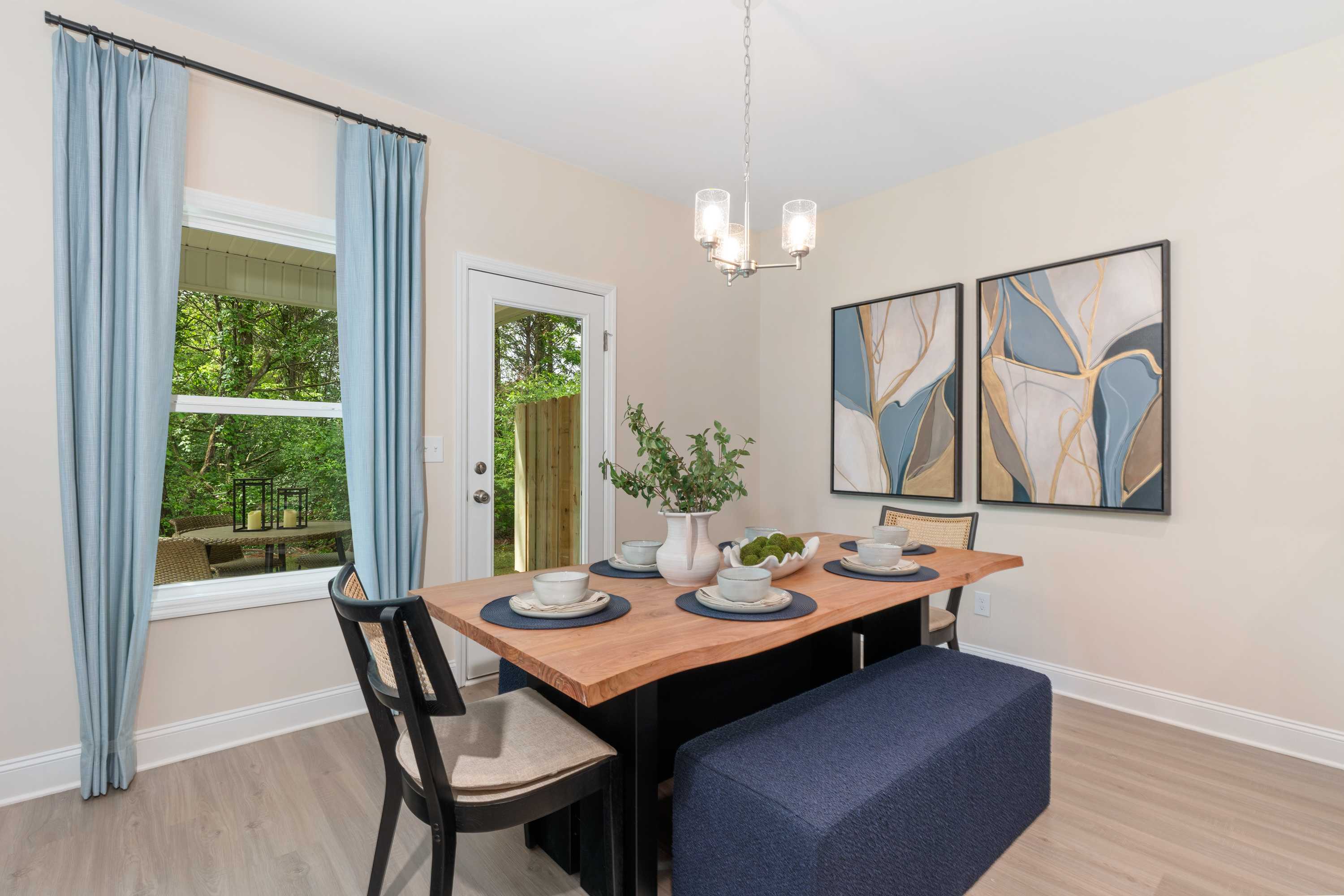 Contemporary dining room at Pavilion in Huntsville AL with rustic wood table, blue curtains, abstract art, and garden view