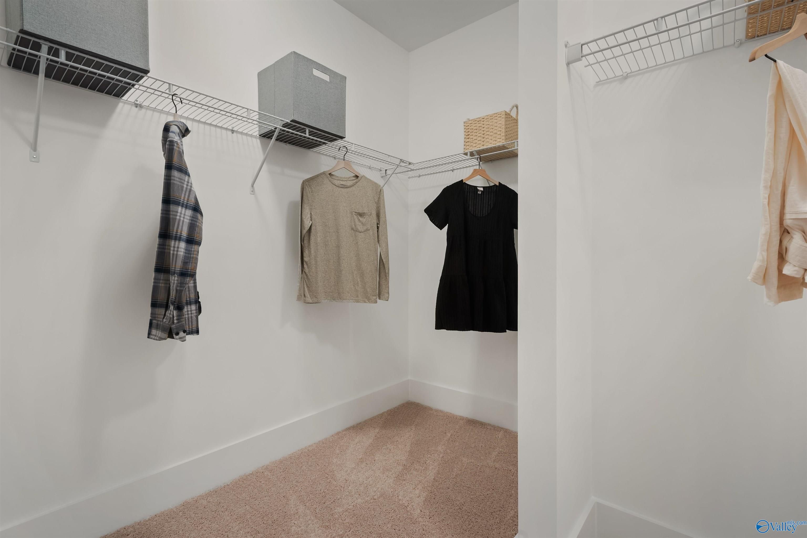 Spacious walk-in closet with hanging clothes, wire shelving, and storage bins in The Everett master suite by Davidson Homes, New Market, Alabama