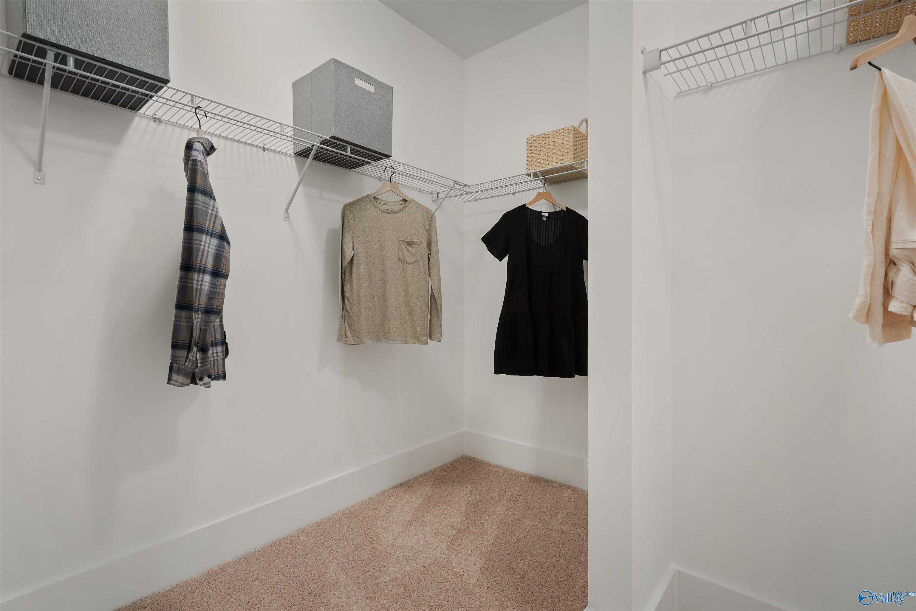 Spacious walk-in closet with hanging clothes, wire shelving, and storage bins in The Everett master suite by Davidson Homes, New Market, Alabama