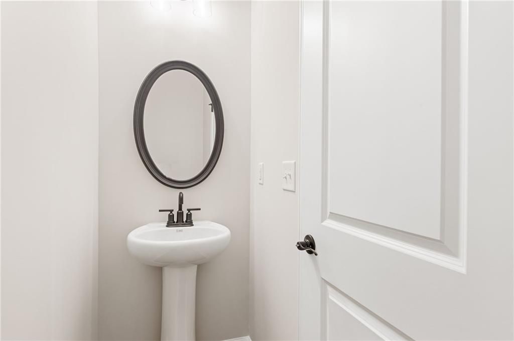 Elegant powder room featuring white pedestal sink and oval mirror in Davidson Homes The Glenwood A, Loganville, Georgia