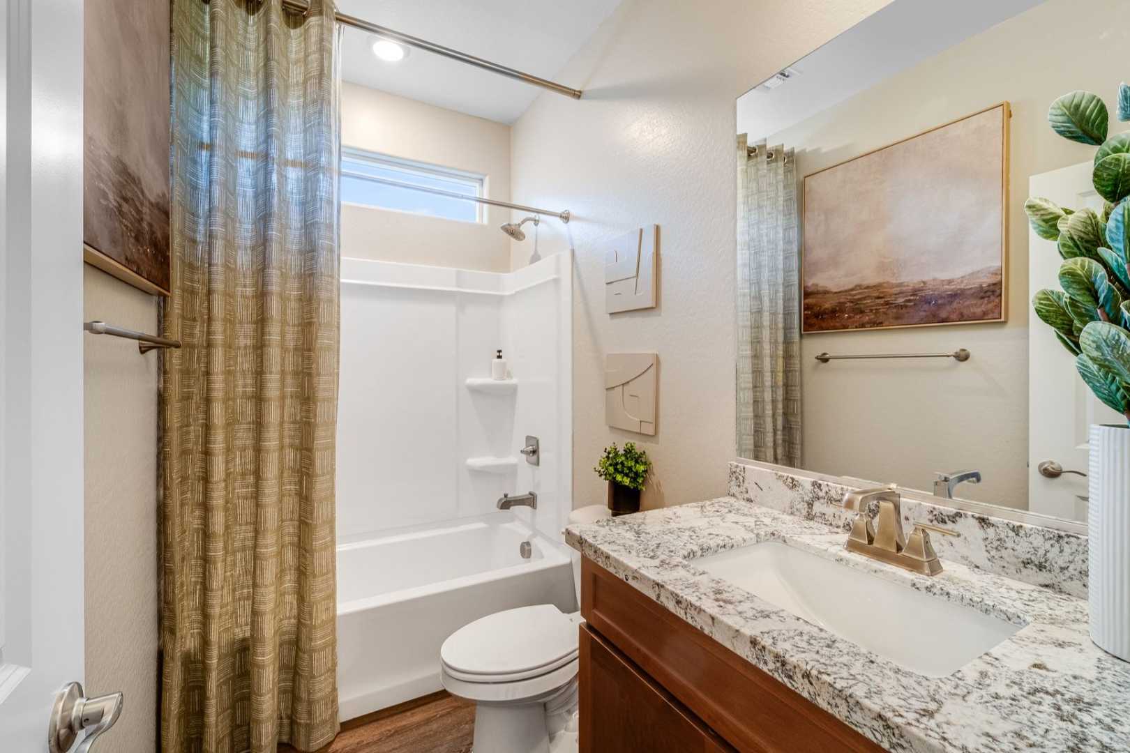 Spacious master bathroom in The Savannah C with white soaking tub, quartz vanity, mirror, potted plants, and neutral decor