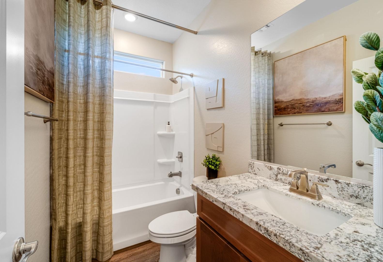 Guest bathroom in The Savannah home design with tub-shower combo, granite vanity, large mirror, and desert artwork