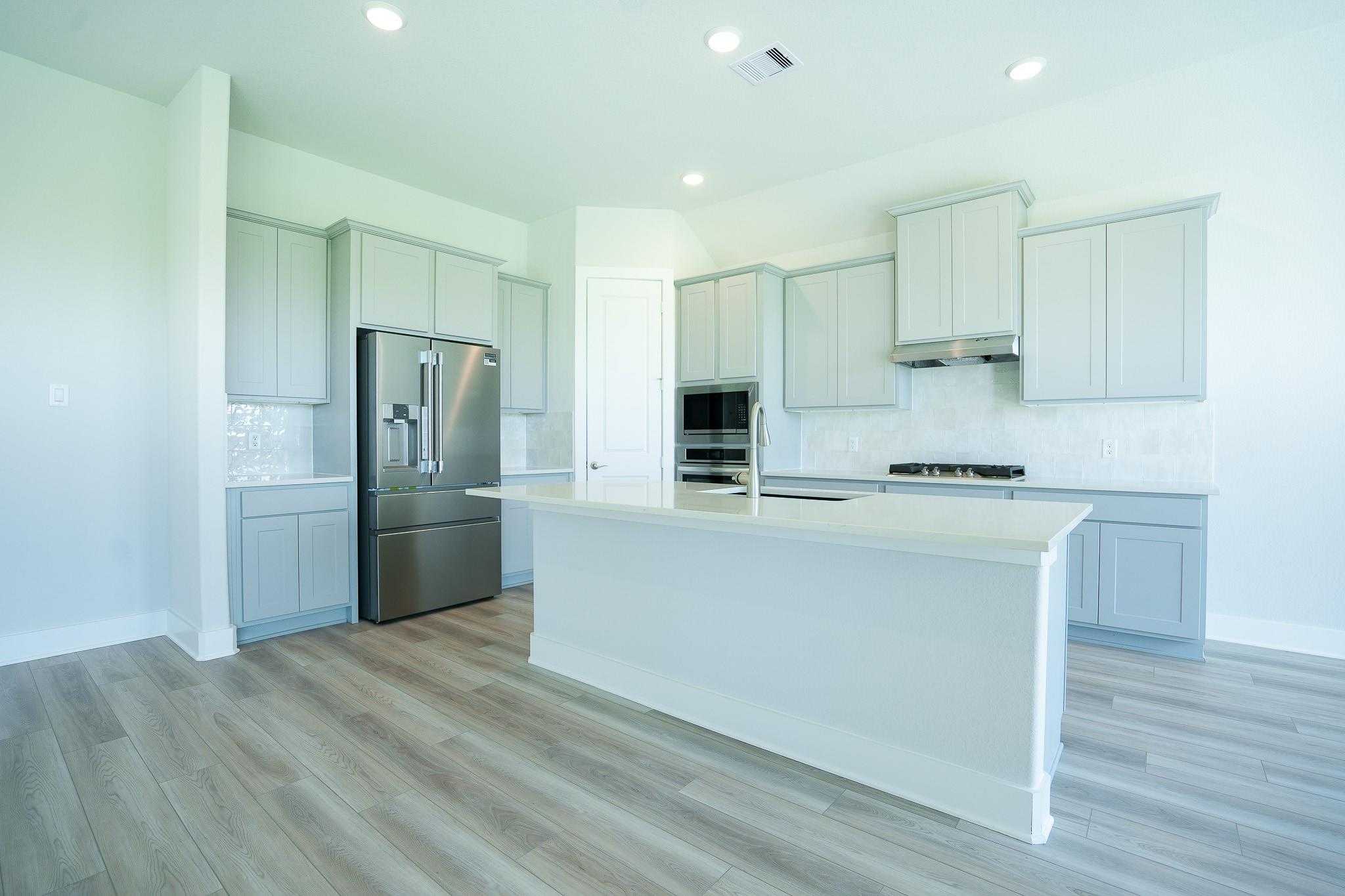 Modern kitchen with white shaker cabinets, stainless steel appliances, large island, and hardwood floors in Davidson Homes The Edward A, Texas City