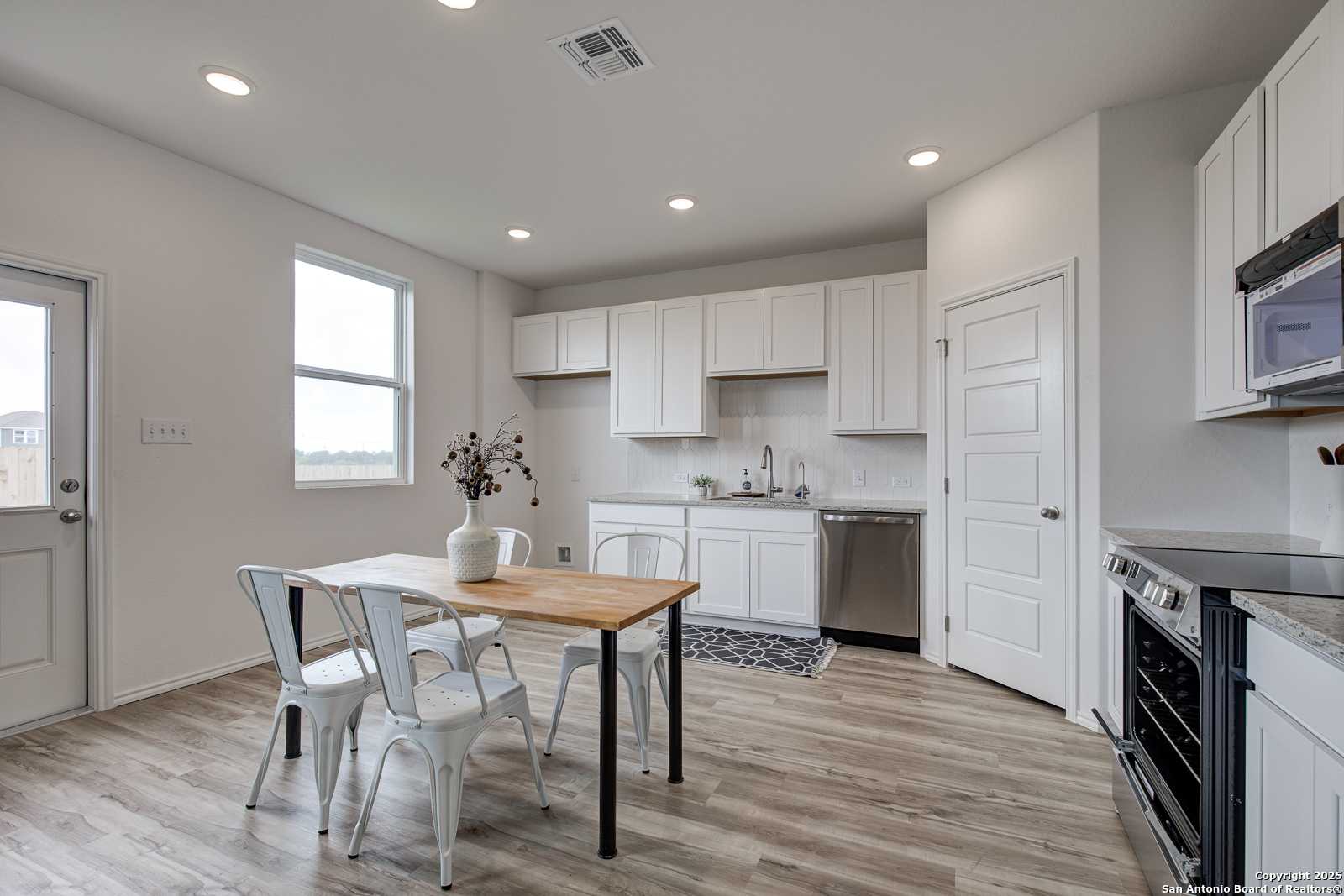 Modern white kitchen with stainless appliances, island bar, and hardwood floors in Davidson Homes The Trinity A, San Antonio