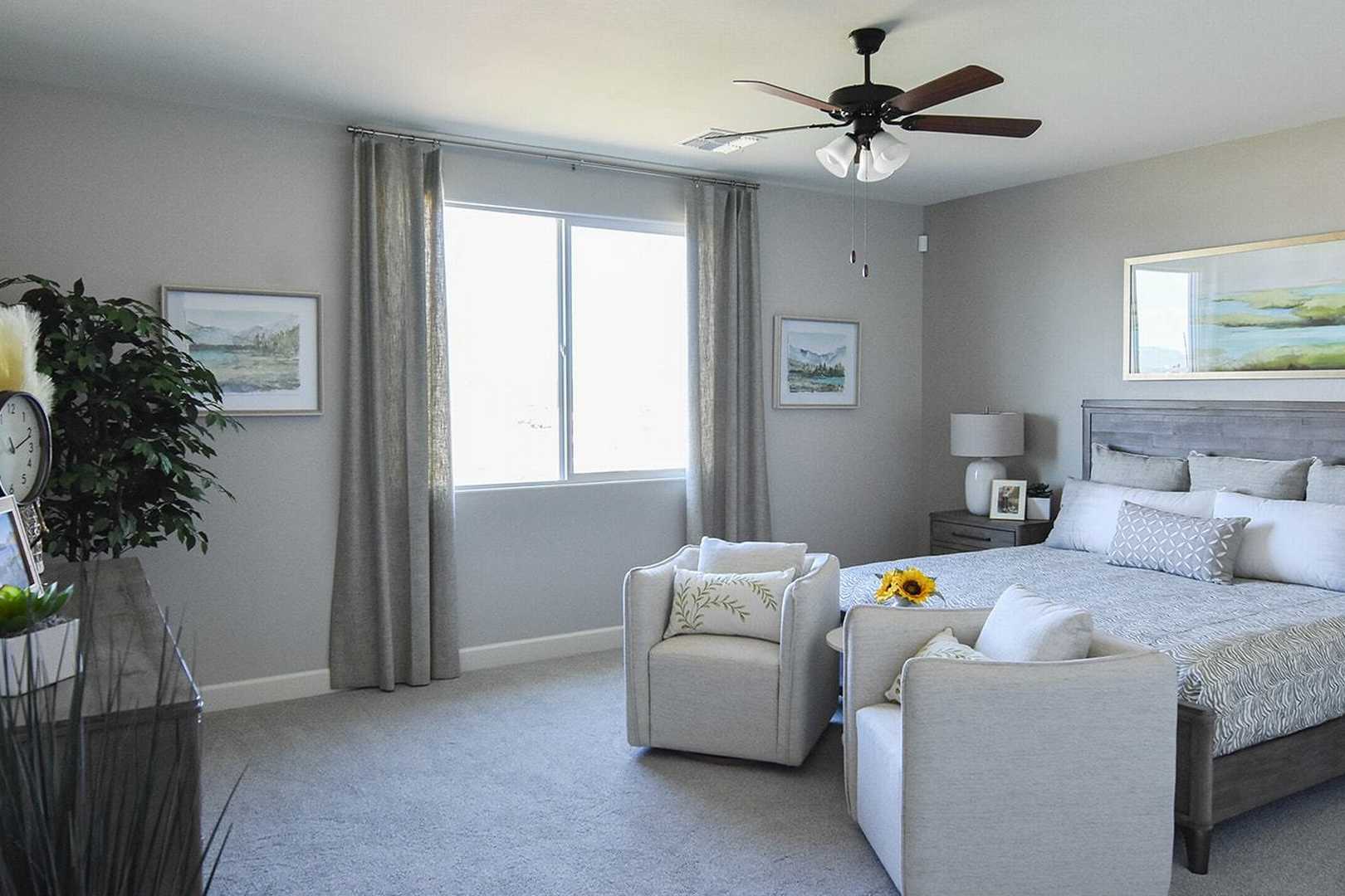 Spacious master bedroom in The Summit B featuring plush king bed, gray walls, armchairs, and large window with sheer curtains