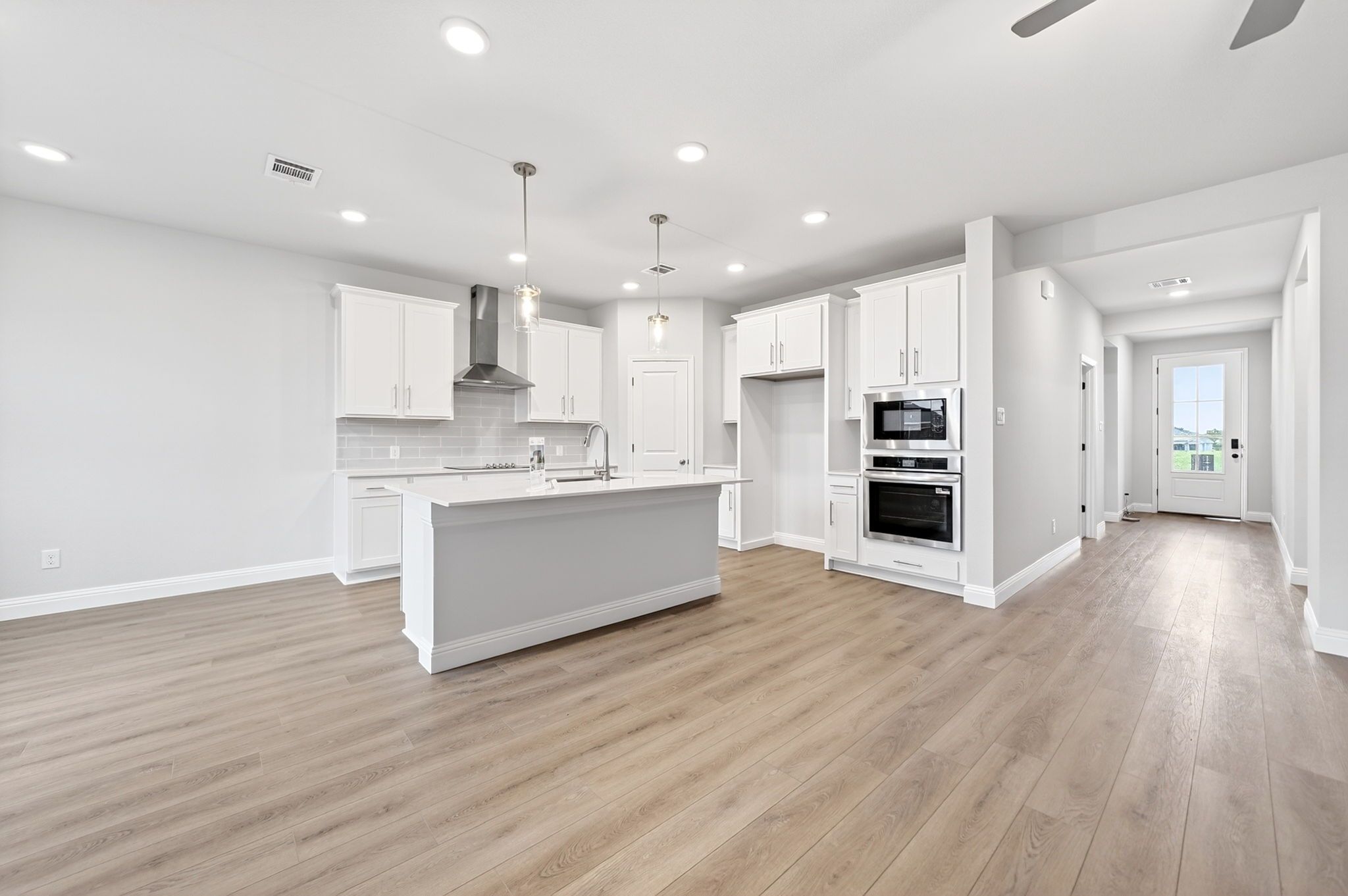 Modern kitchen in The Redbud home design featuring white cabinetry, a spacious island, and stainless steel appliances.