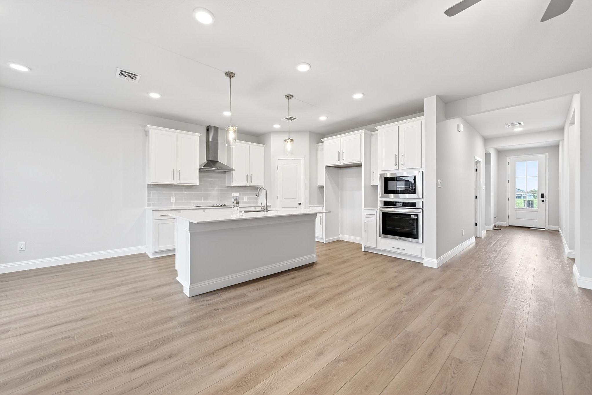 Modern kitchen in The Redbud home design featuring white cabinetry, a spacious island, and stainless steel appliances.