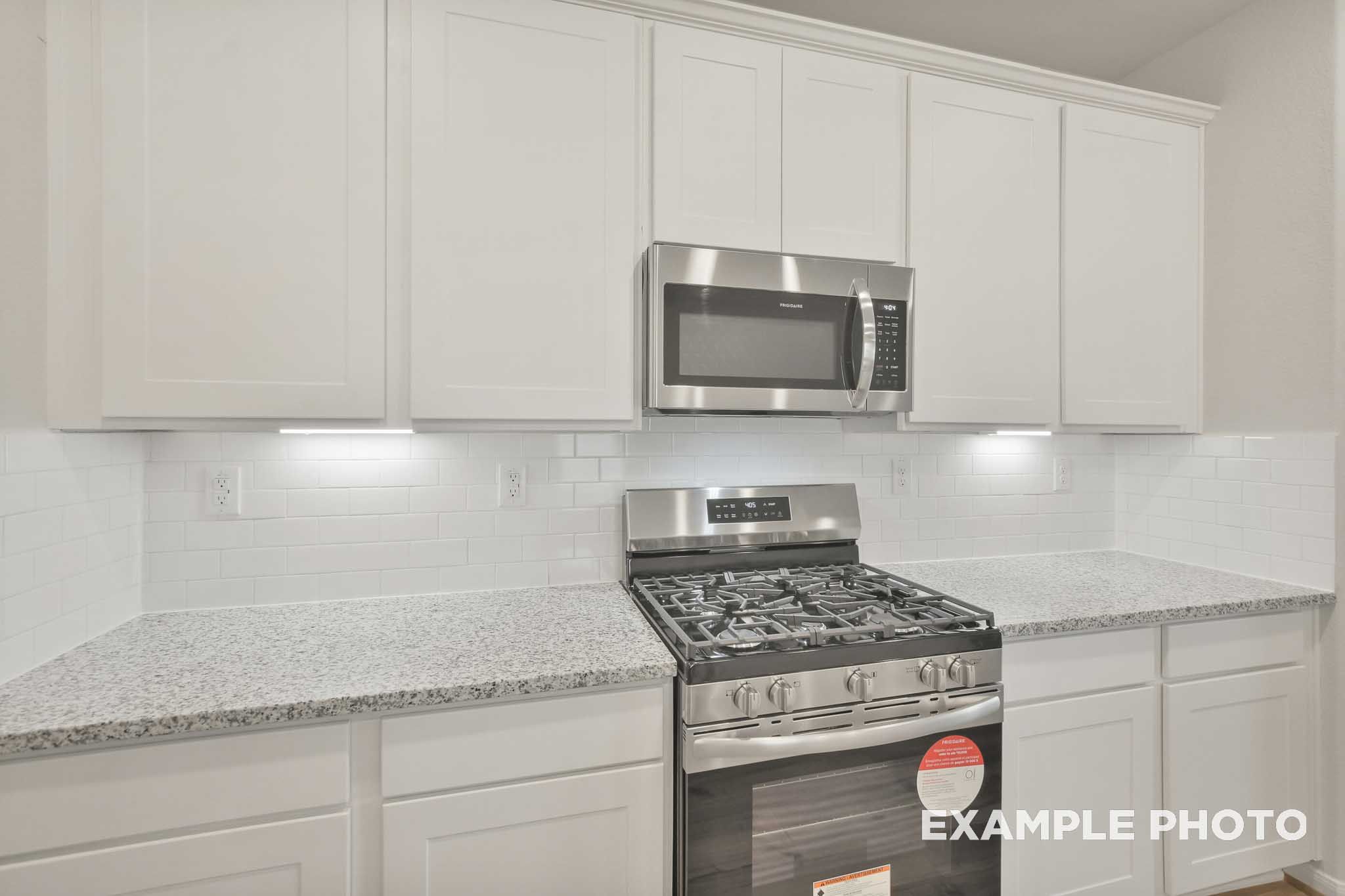 Kitchen in The Brazos by Davidson Homes featuring white shaker cabinets, granite countertops, gas range, and microwave