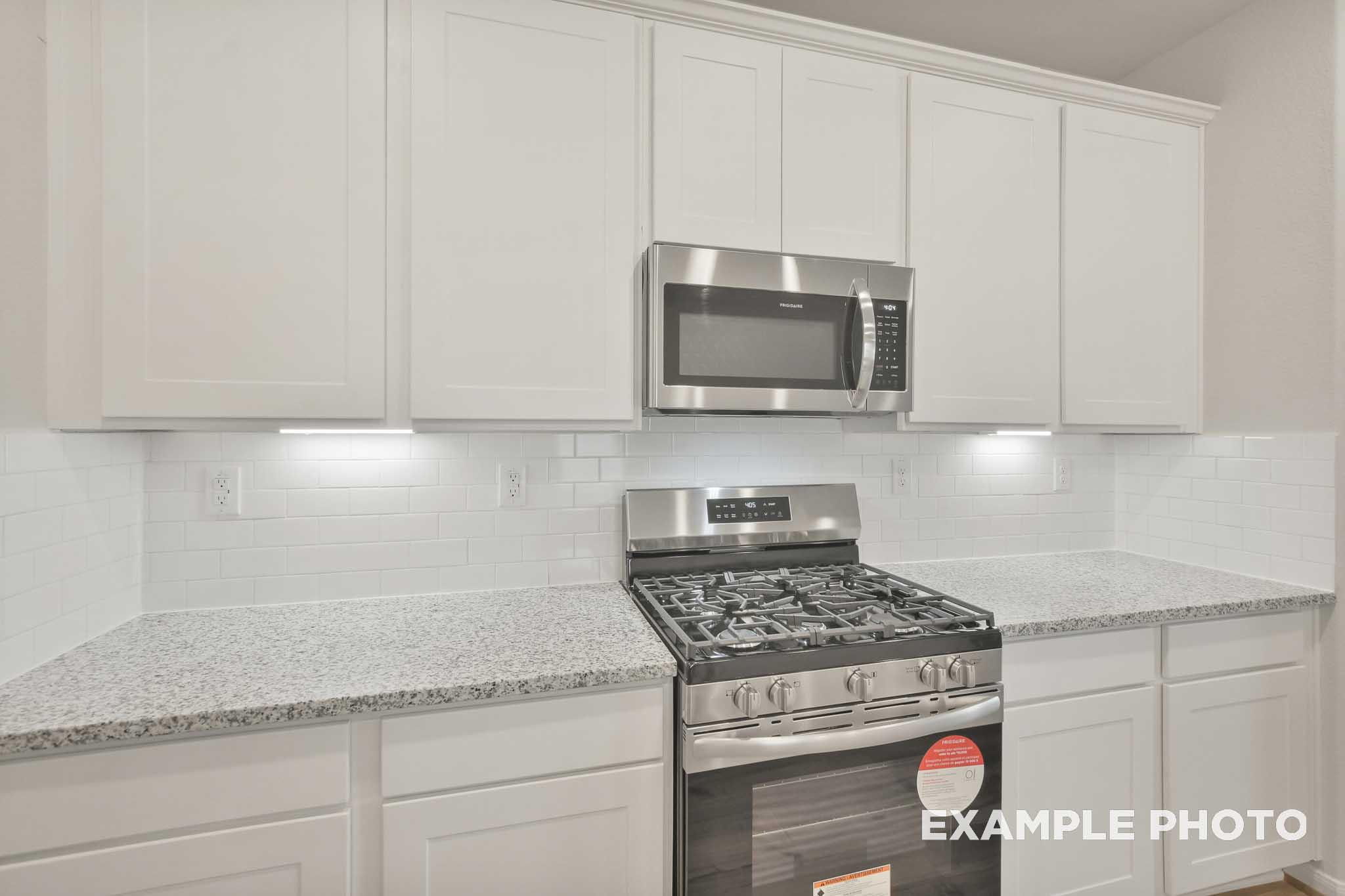 Kitchen in The Brazos by Davidson Homes featuring white shaker cabinets, granite countertops, gas range, and microwave