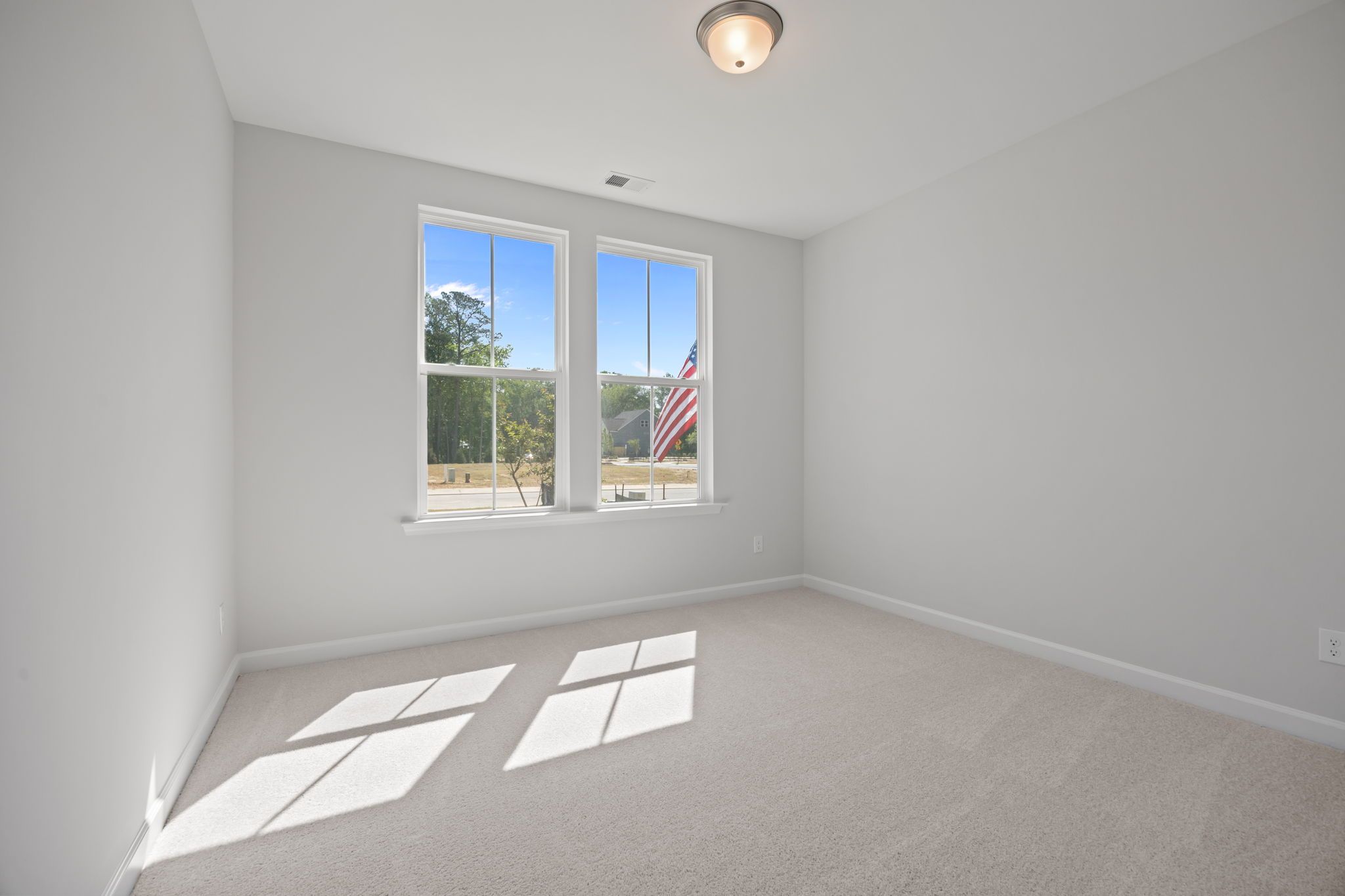 Bright, carpeted bedroom in The Ashport C floor plan by Davidson Homes with natural light and large windows.