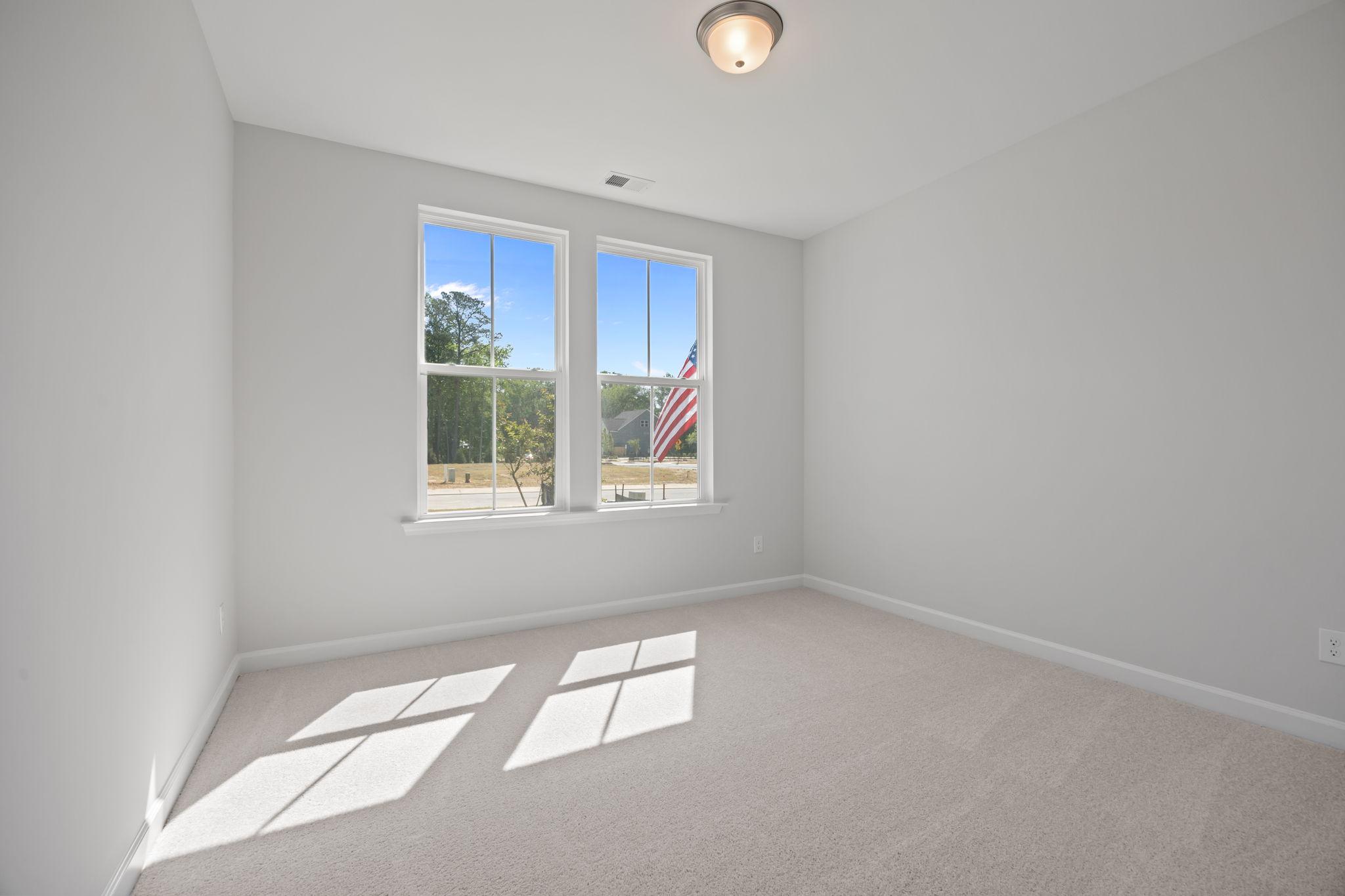 Bright, carpeted bedroom in The Ashport B floor plan by Davidson Homes featuring large windows and neutral wall colors.