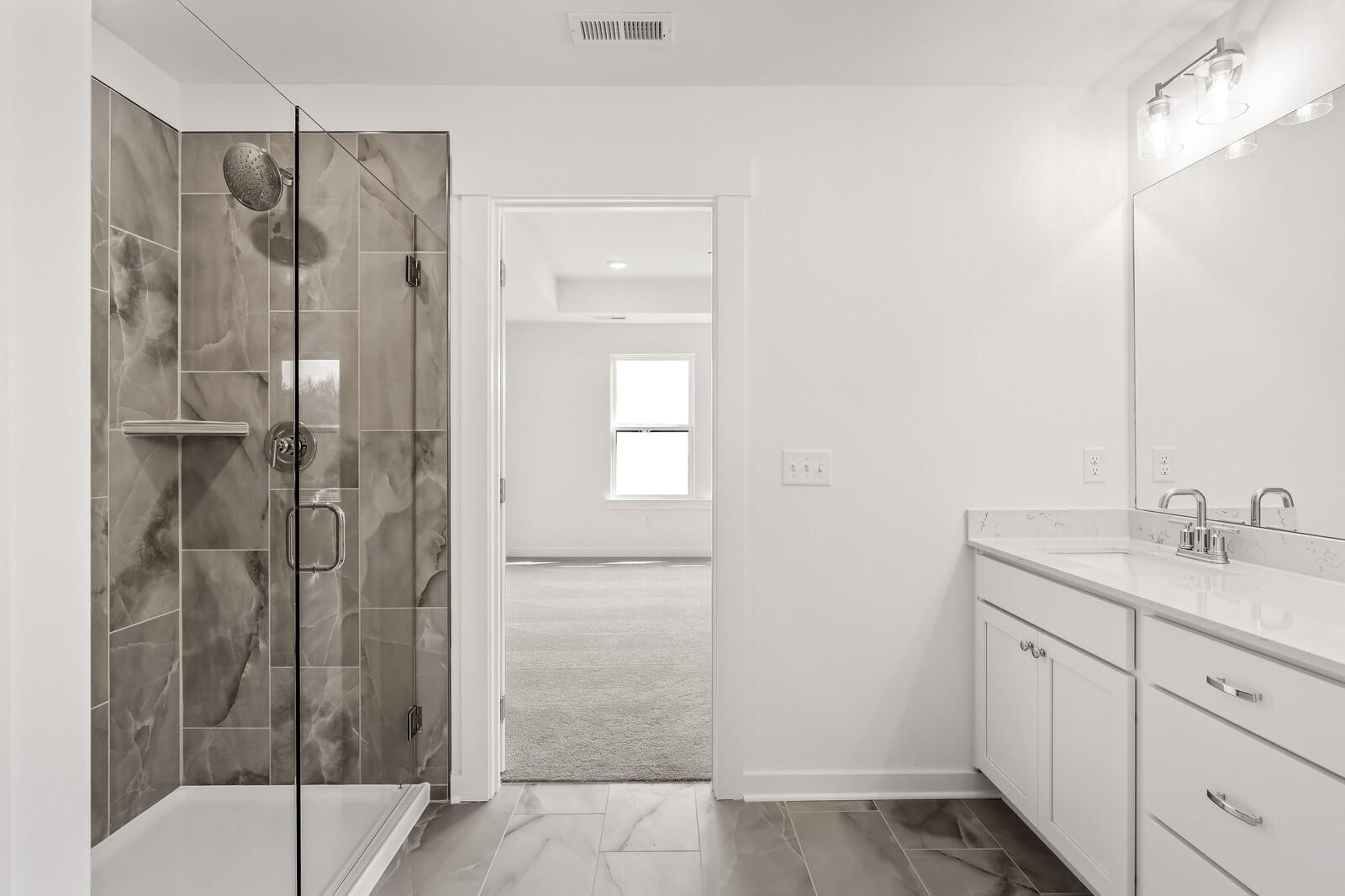 Modern master bath with frameless glass shower, gray tile, double white vanity in Davidson Homes The Willow D, Mt. Juliet, TN