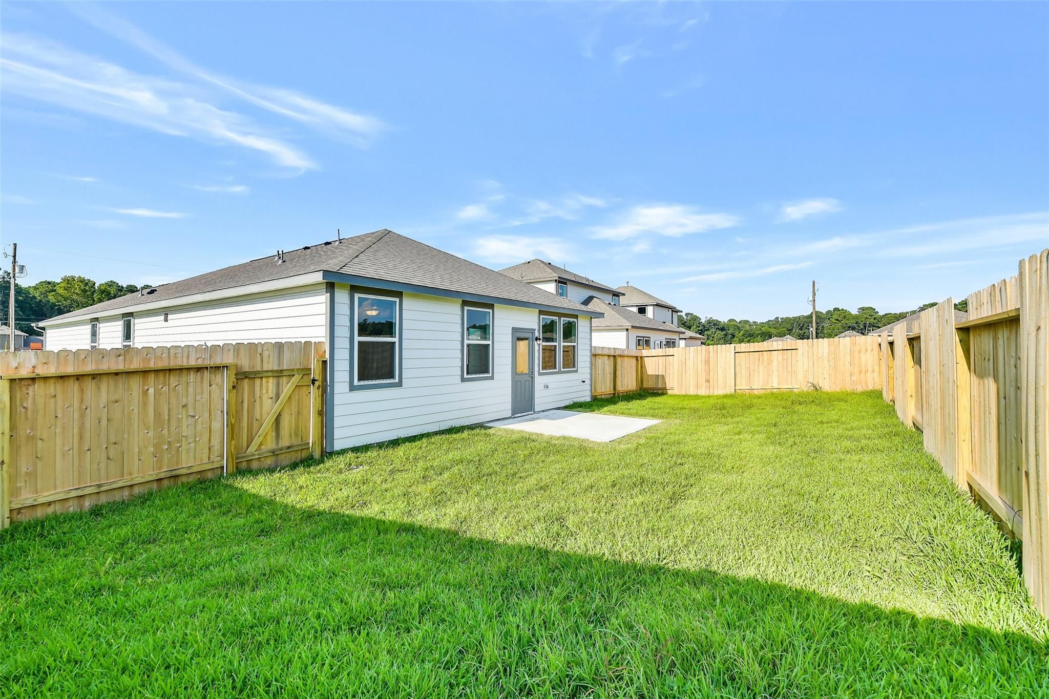 Spacious fenced backyard with lush green grass and concrete patio behind white single-story Davidson Homes in Liberty Estates, Cleveland, Texas