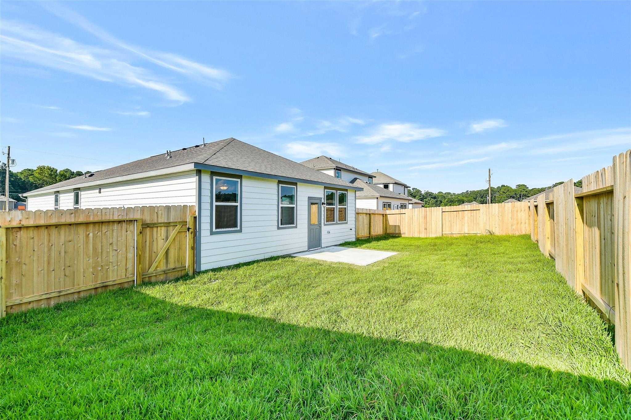 Fenced private backyard with lush green lawn and white-sided home in Davidson Homes The Colorado F, Liberty Estates, Cleveland, Texas