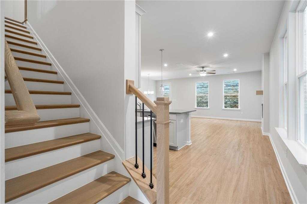 Open foyer featuring oak staircase with black metal railing and adjacent modern kitchen island in The Cary A, Kennesaw, GA