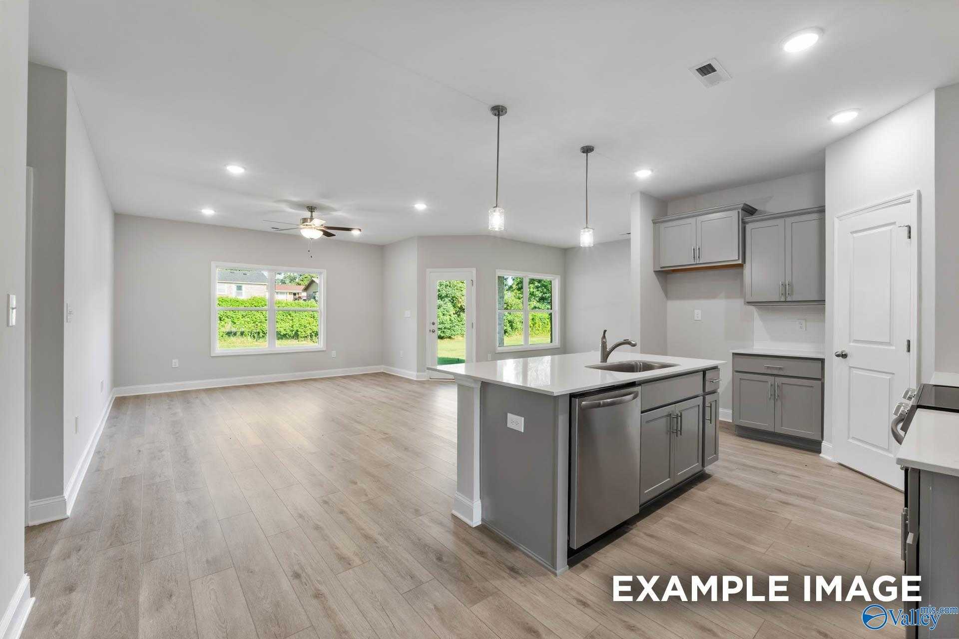 Open-concept kitchen with gray island, stainless sink, pendant lights, and backyard views in Davidson Homes The Daphne C, New Market, AL