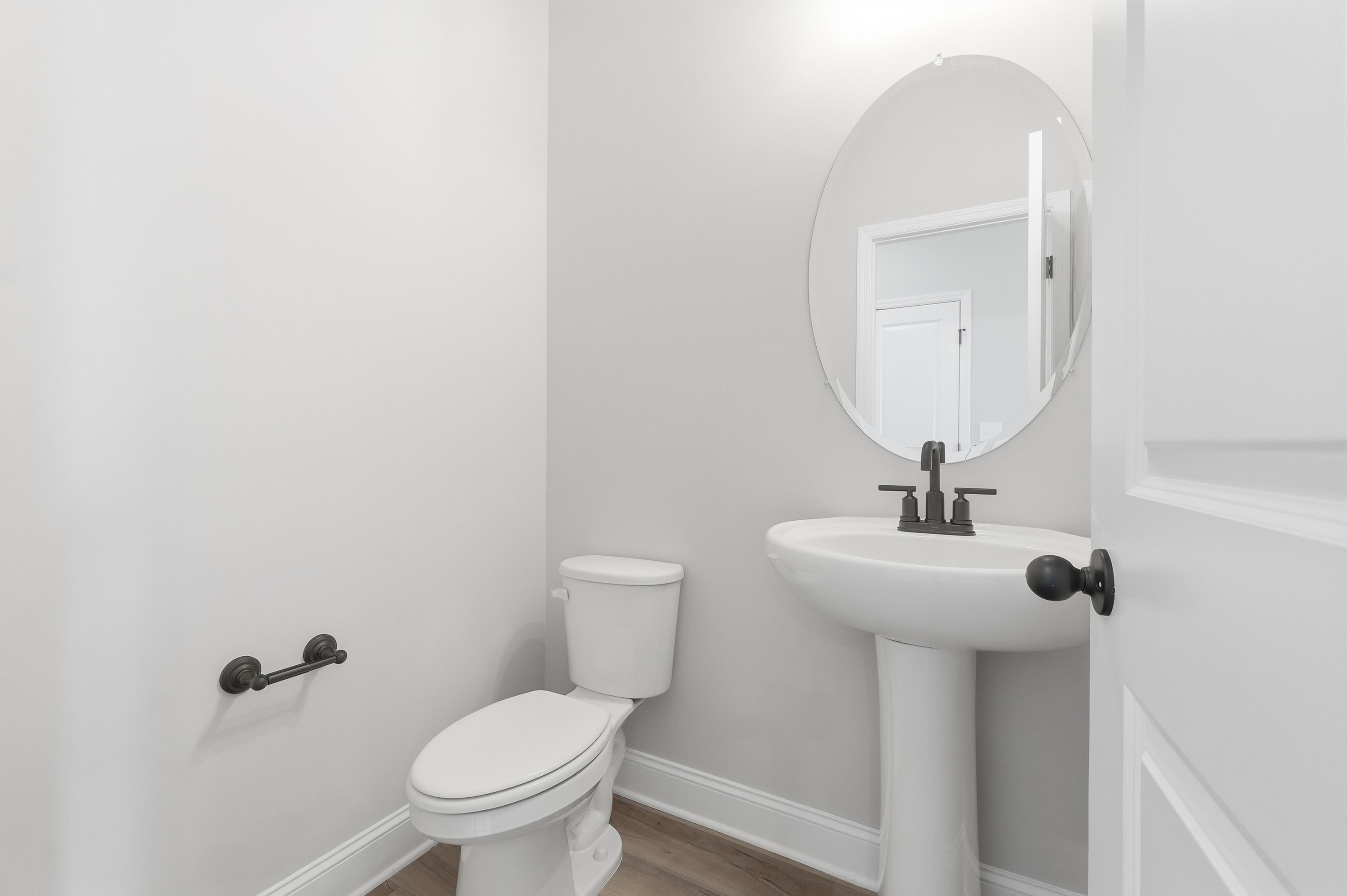 Modern powder room in The Rockford by Davidson Homes featuring white pedestal sink, round mirror, and black fixtures