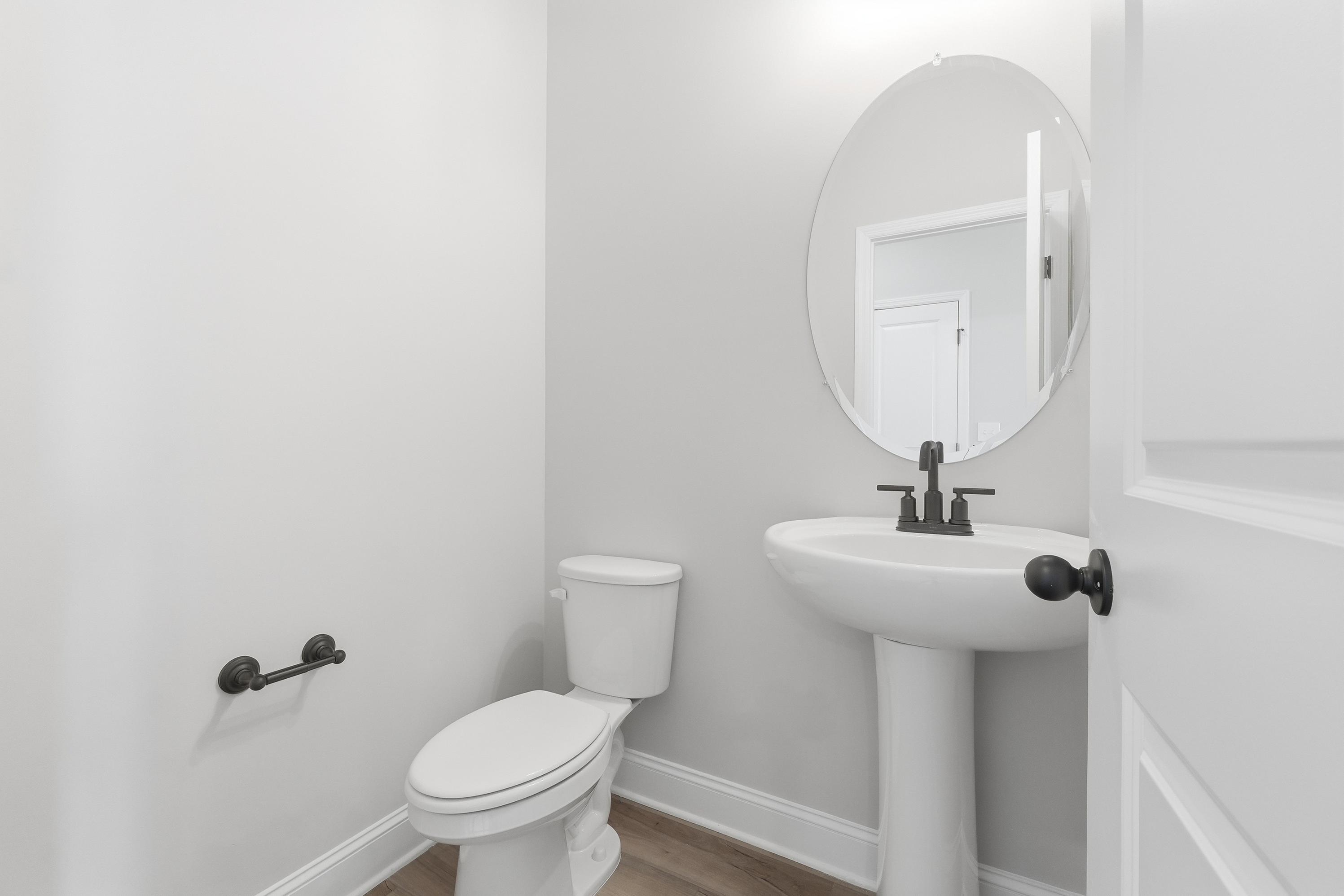 Modern powder room in The Rockford by Davidson Homes featuring white pedestal sink, round mirror, and black fixtures