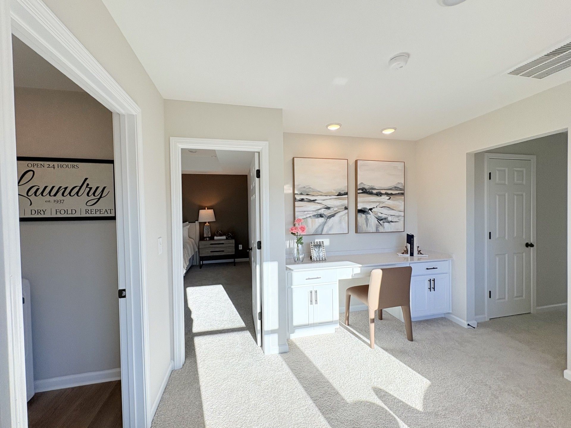 Modern laundry room in Hemingway Cumming GA home by Davidson Homes with washer dryer, desk nook, abstract art, and bedroom view