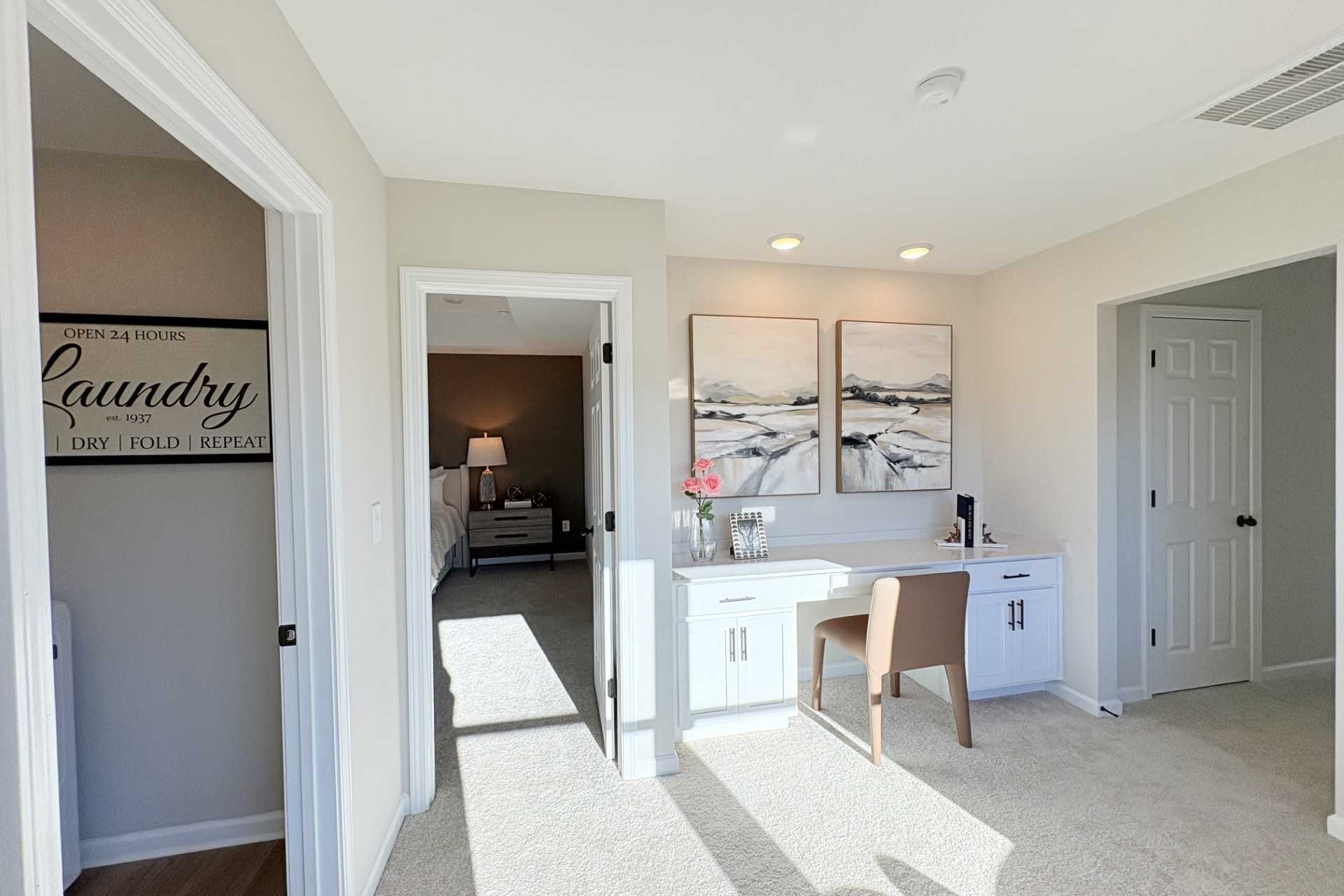 Modern laundry room in Hemingway Cumming GA home by Davidson Homes with washer dryer, desk nook, abstract art, and bedroom view
