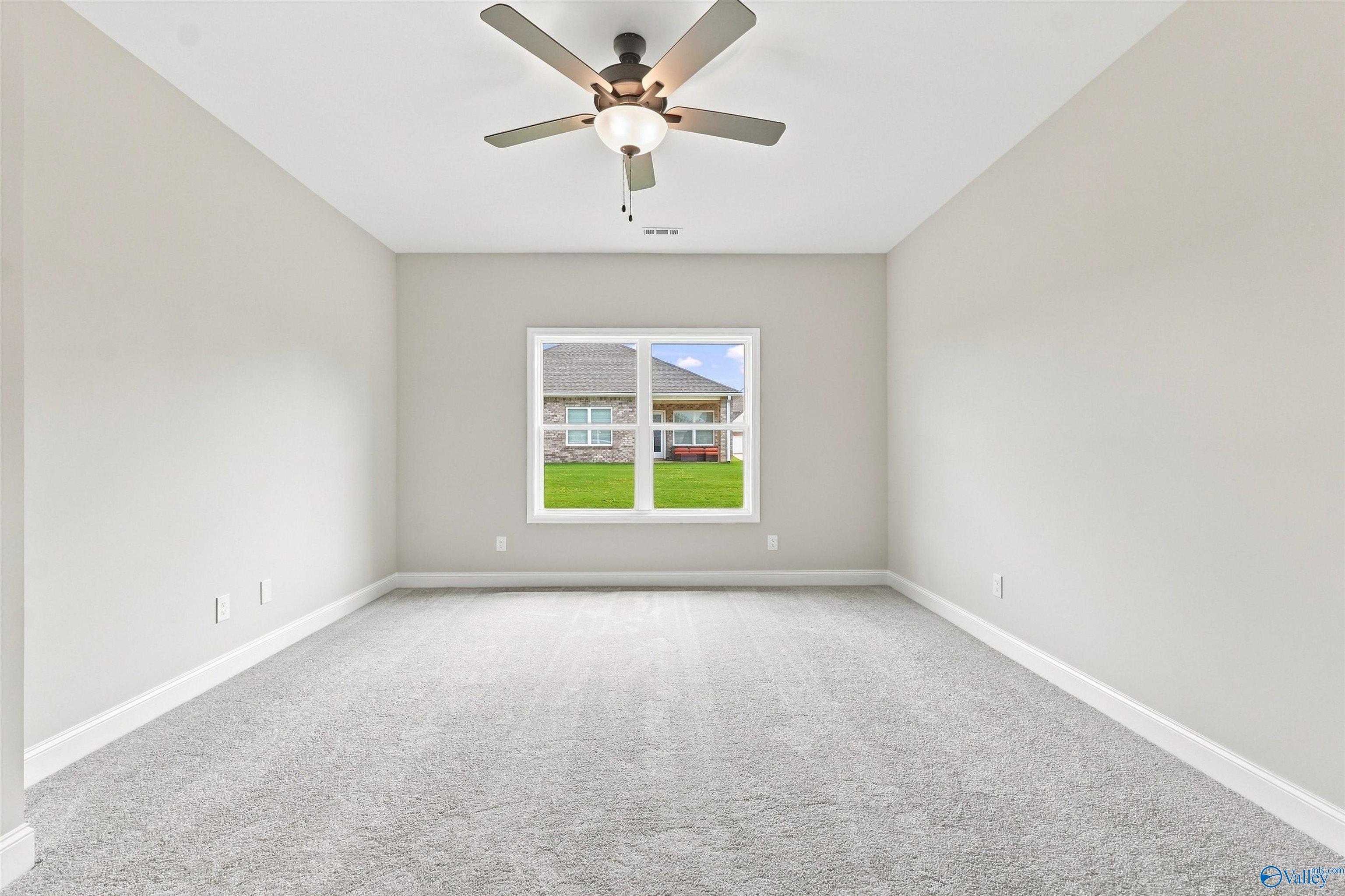 Spacious carpeted bedroom with ceiling fan and window overlooking backyard in Davidson Homes Everett B plan, Toney, Alabama