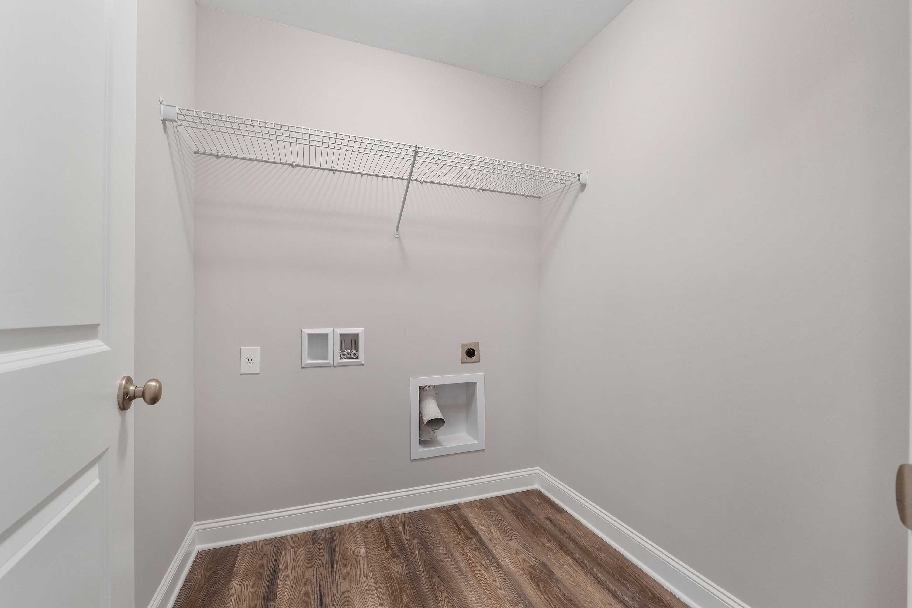 Spacious laundry room in The Aiken by Davidson Homes with wire shelving, washer-dryer hookups, and hardwood floors