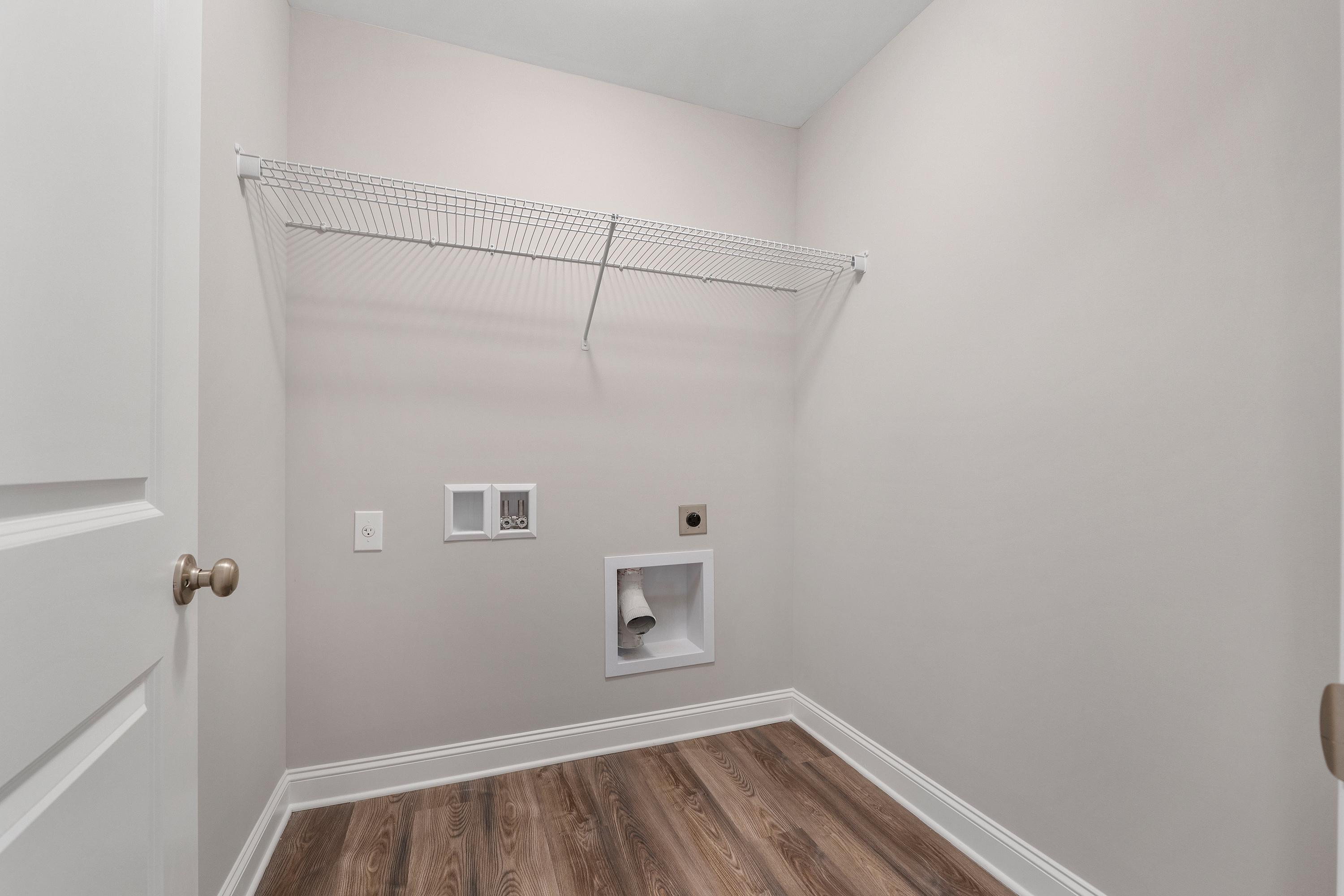Spacious laundry room in The Aiken by Davidson Homes with wire shelving, washer-dryer hookups, and hardwood floors