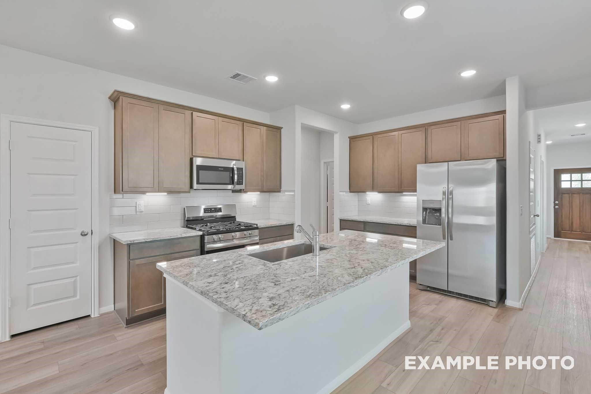Modern kitchen with granite island, stainless appliances, oak cabinets in Davidson Homes The Frio F, Conroe, TX