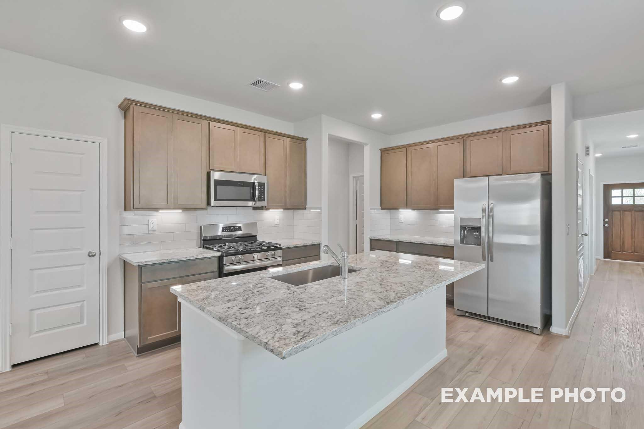 Modern kitchen with granite island, stainless appliances, oak cabinets in Davidson Homes The Frio F, Conroe, TX