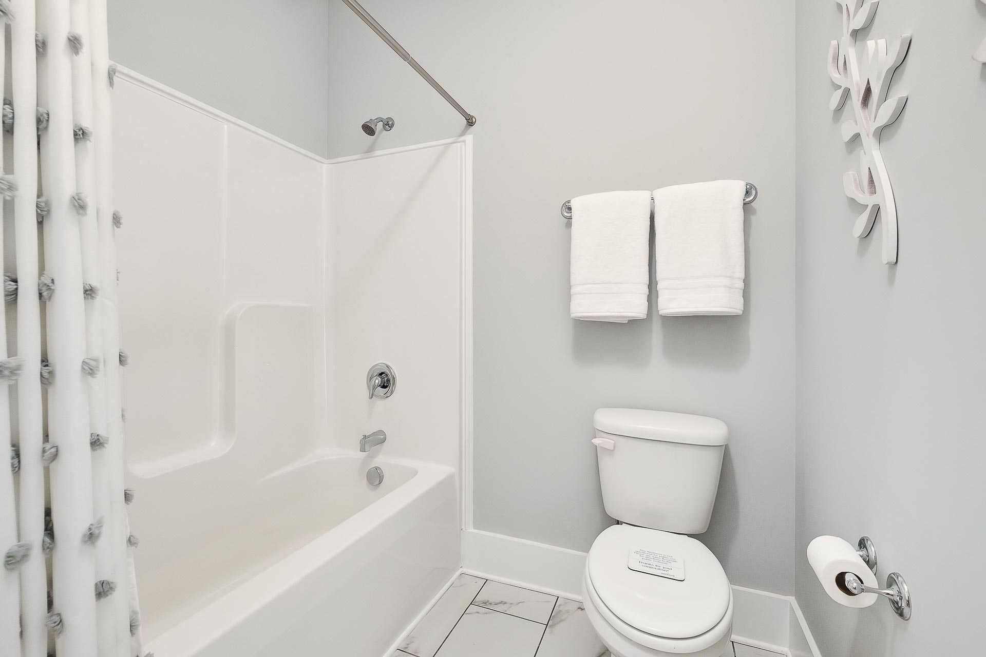 Spacious bathroom in Newby Chapel Athens AL with white bathtub shower combo, toilet, gray walls, towels, and seashell decor