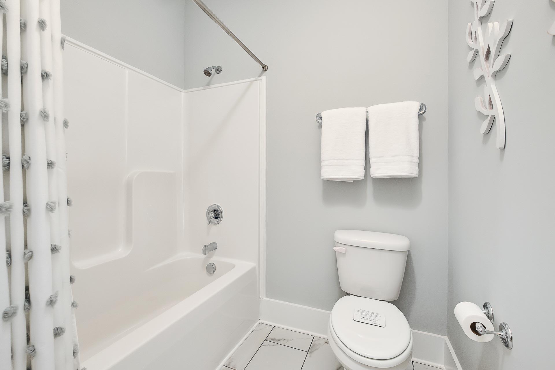 Spacious bathroom in Newby Chapel Athens AL with white bathtub shower combo, toilet, gray walls, towels, and seashell decor