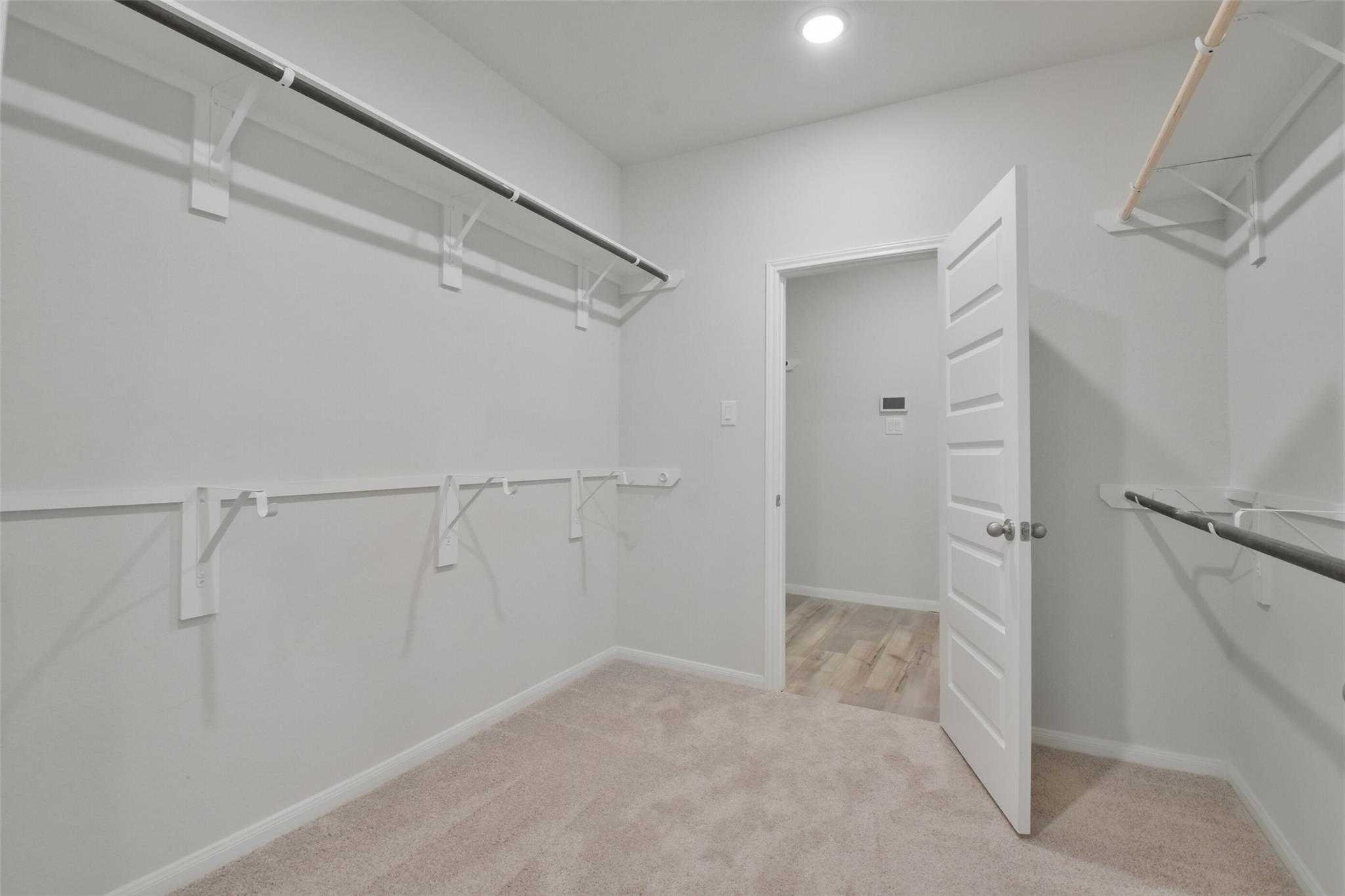Spacious walk-in closet with white walls, hanging rods, and beige carpet in Davidson Homes The Tierra A master suite, Dayton, Texas