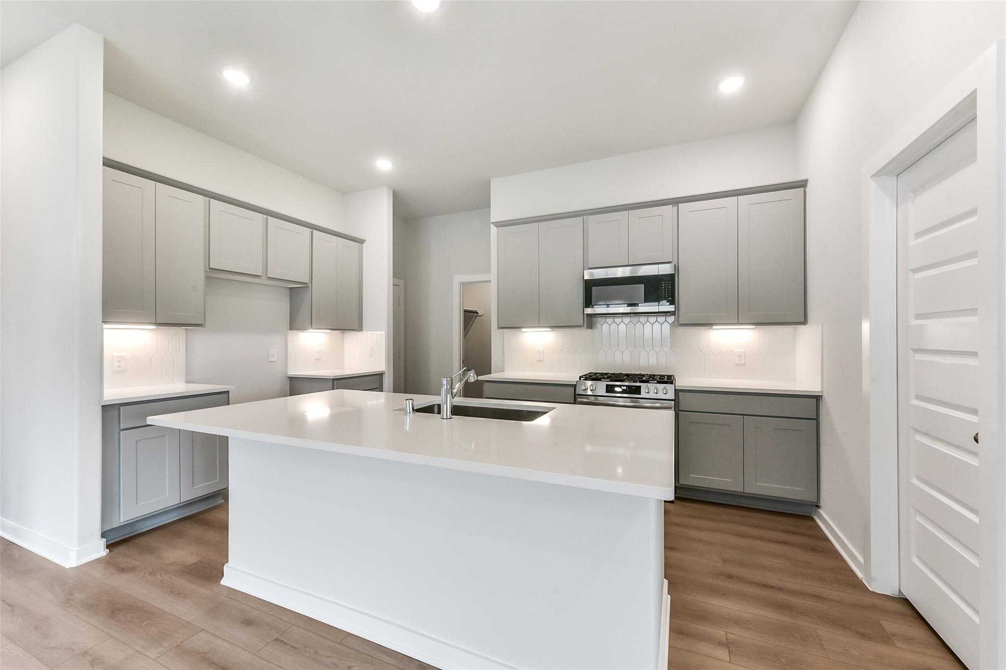 Modern open-concept kitchen with white quartz island, gray cabinets, stainless appliances in Davidson Homes Laguna C, Rosharon, Texas