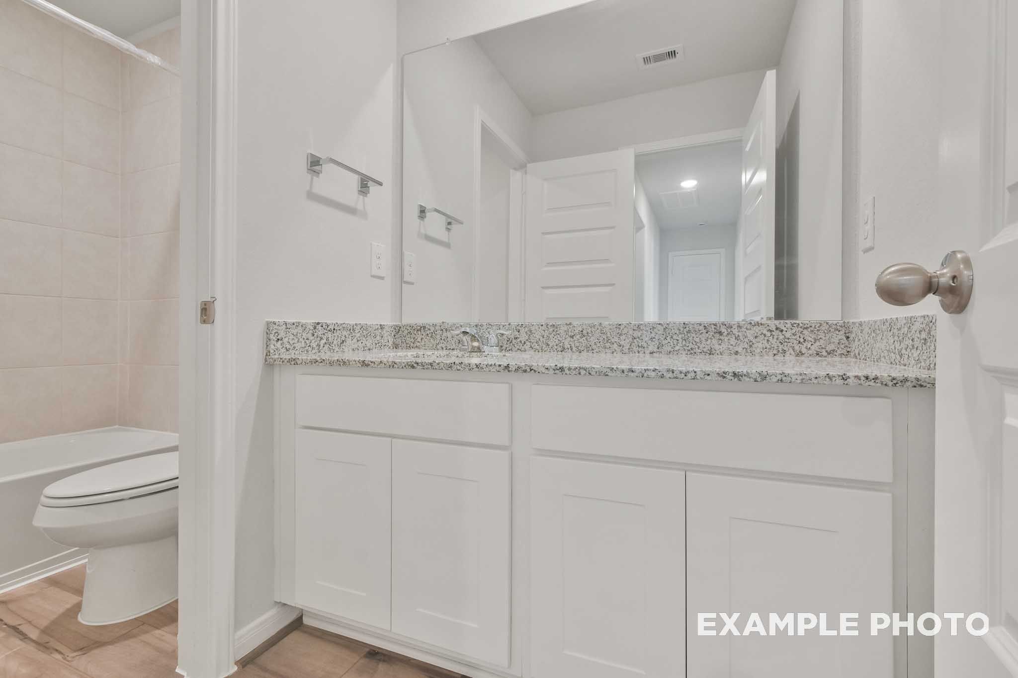 Bright bathroom in The Brazos by Davidson Homes featuring white vanity, granite countertop, and tub shower combo