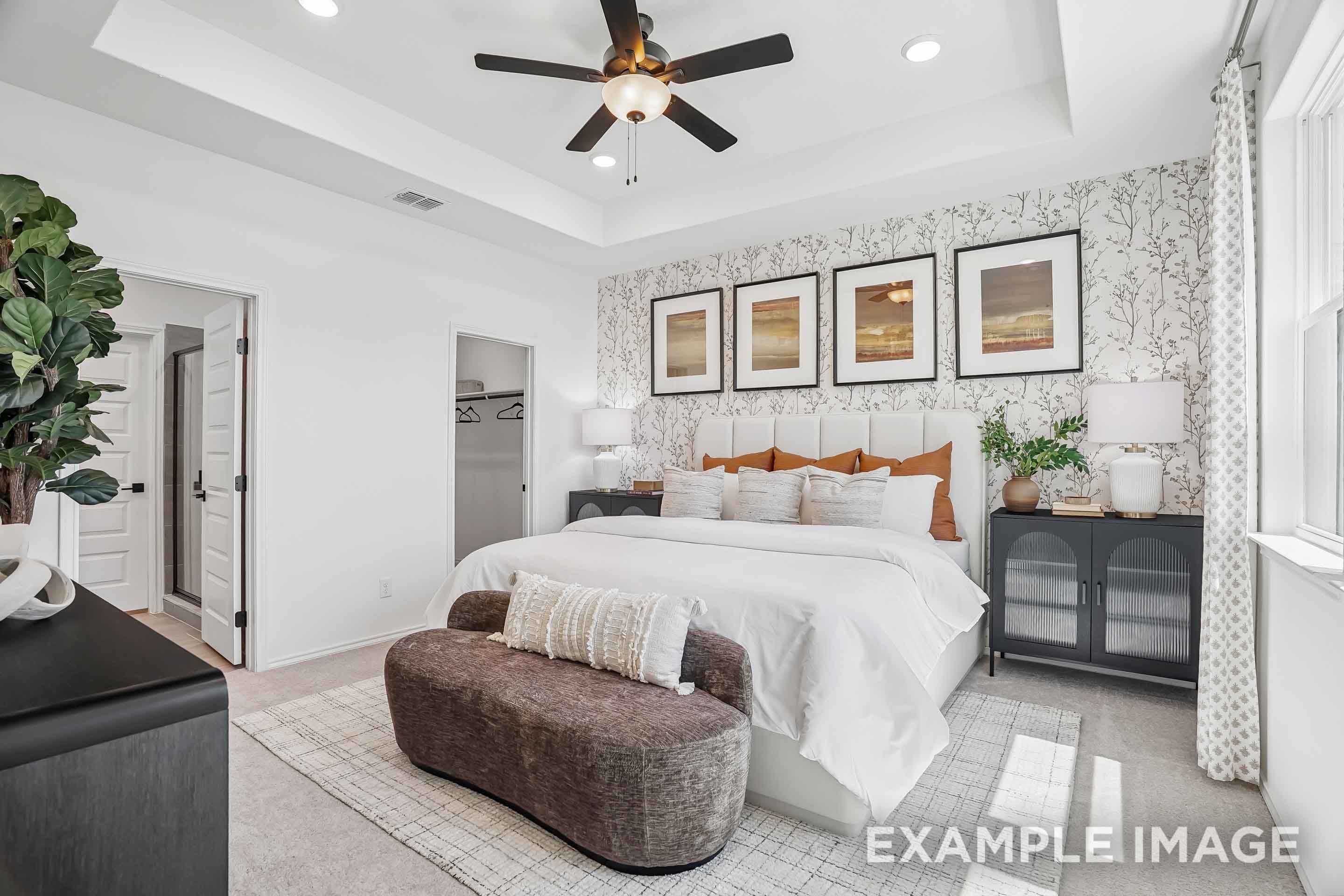 Spacious master suite on main floor of The Pinecrest D featuring tray ceiling, plush bedding, and modern accent wall.