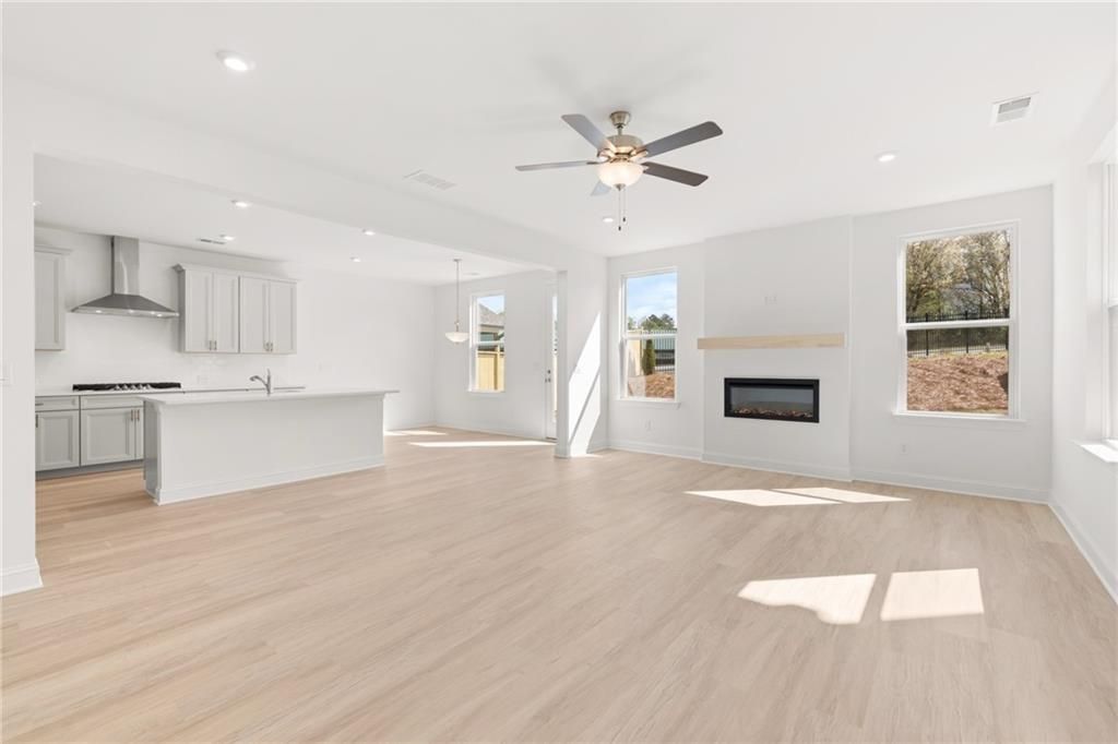 Open-concept living room with gas fireplace, white kitchen island, and large windows in The Gavin E, Kennesaw, Georgia