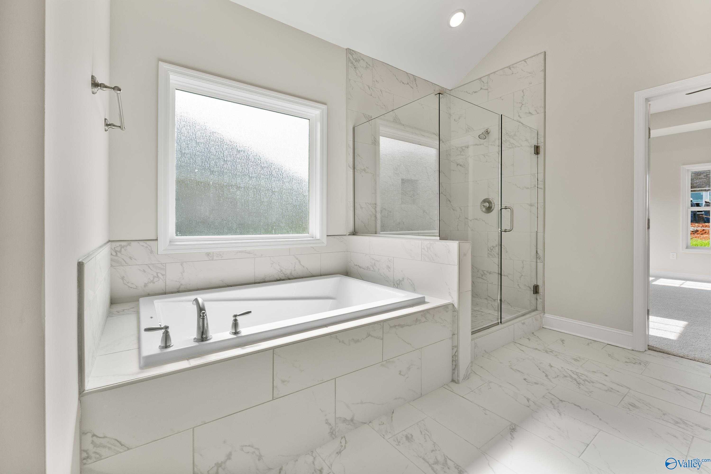 Elegant master bathroom with freestanding tub, frameless glass shower, marble tiles in Davidson Homes The Finleigh, Toney, Alabama