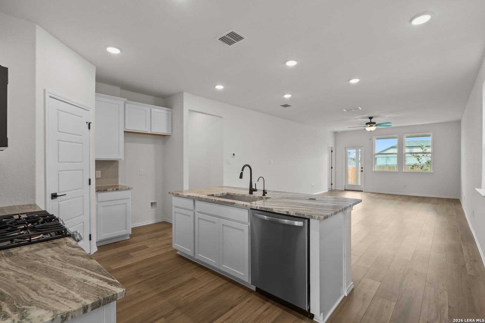 White shaker kitchen island with granite countertops, stainless dishwasher, and hardwood floors in Davidson Homes Summit B, San Antonio