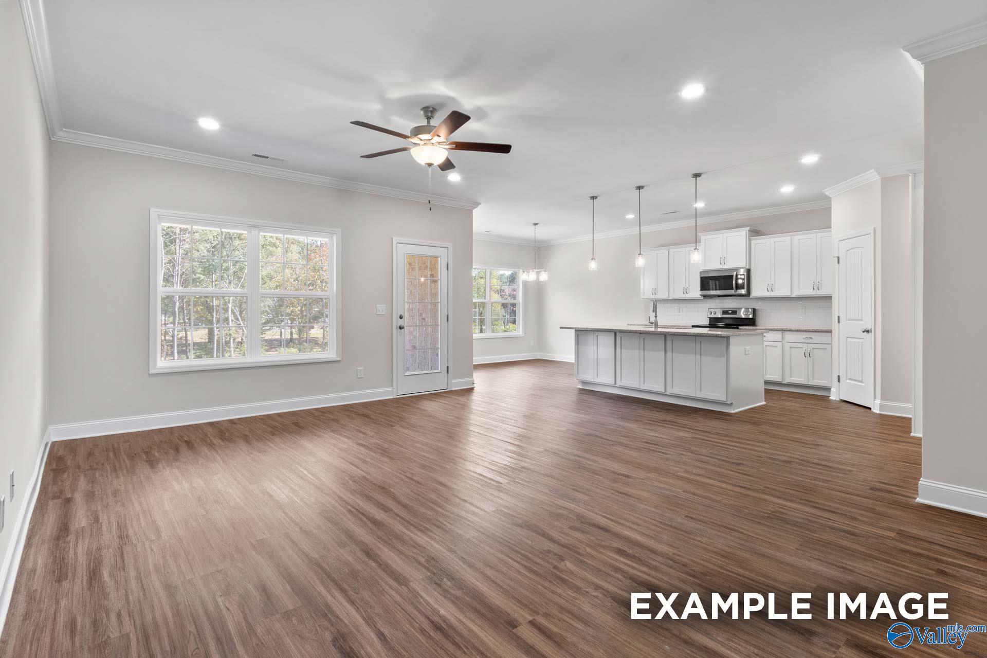 Spacious open-concept living and kitchen with hardwood floors, white cabinets, ceiling fan, and large windows in Davidson Homes The Montgomery C, Harvest, Alabama