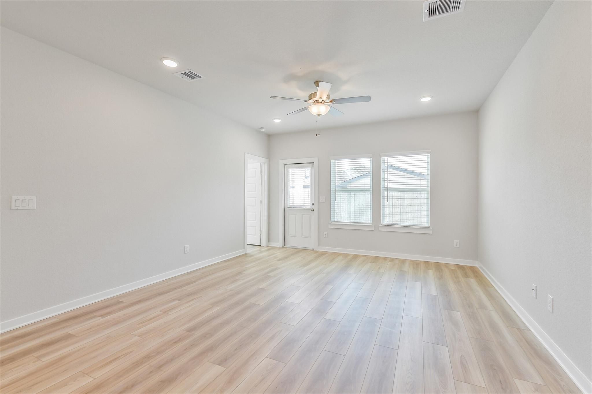 Spacious living room with light oak floors, ceiling fan, and large windows in Davidson Homes Rio Grande H, Magnolia TX