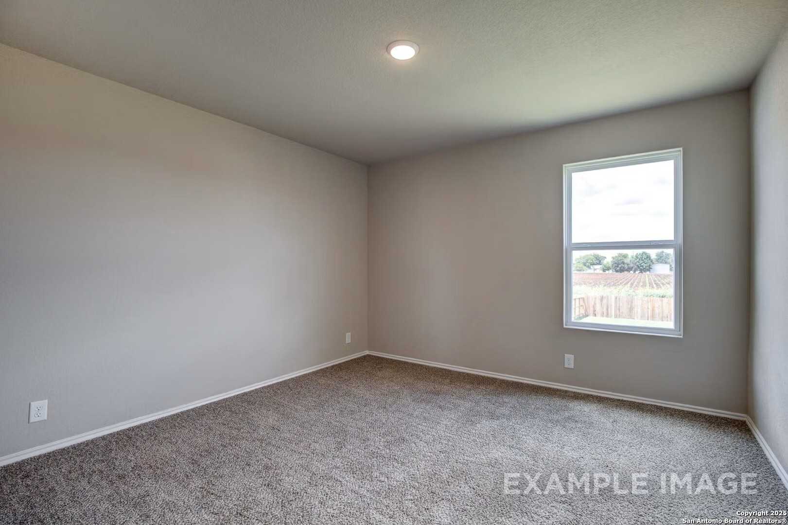 Spacious empty bedroom with neutral gray walls, plush carpet, and large window in Davidson Homes The Murray K, San Antonio
