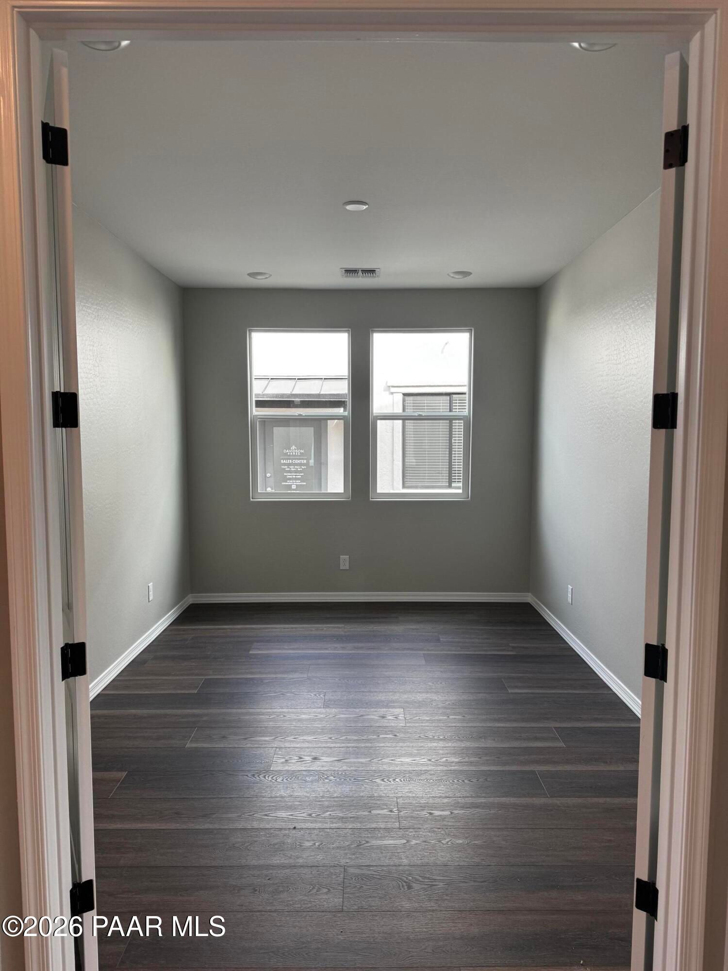 Spacious empty bedroom with light gray walls, large dual windows, blinds, and dark hardwood floors in Davidson Homes Durango II B, Prescott AZ