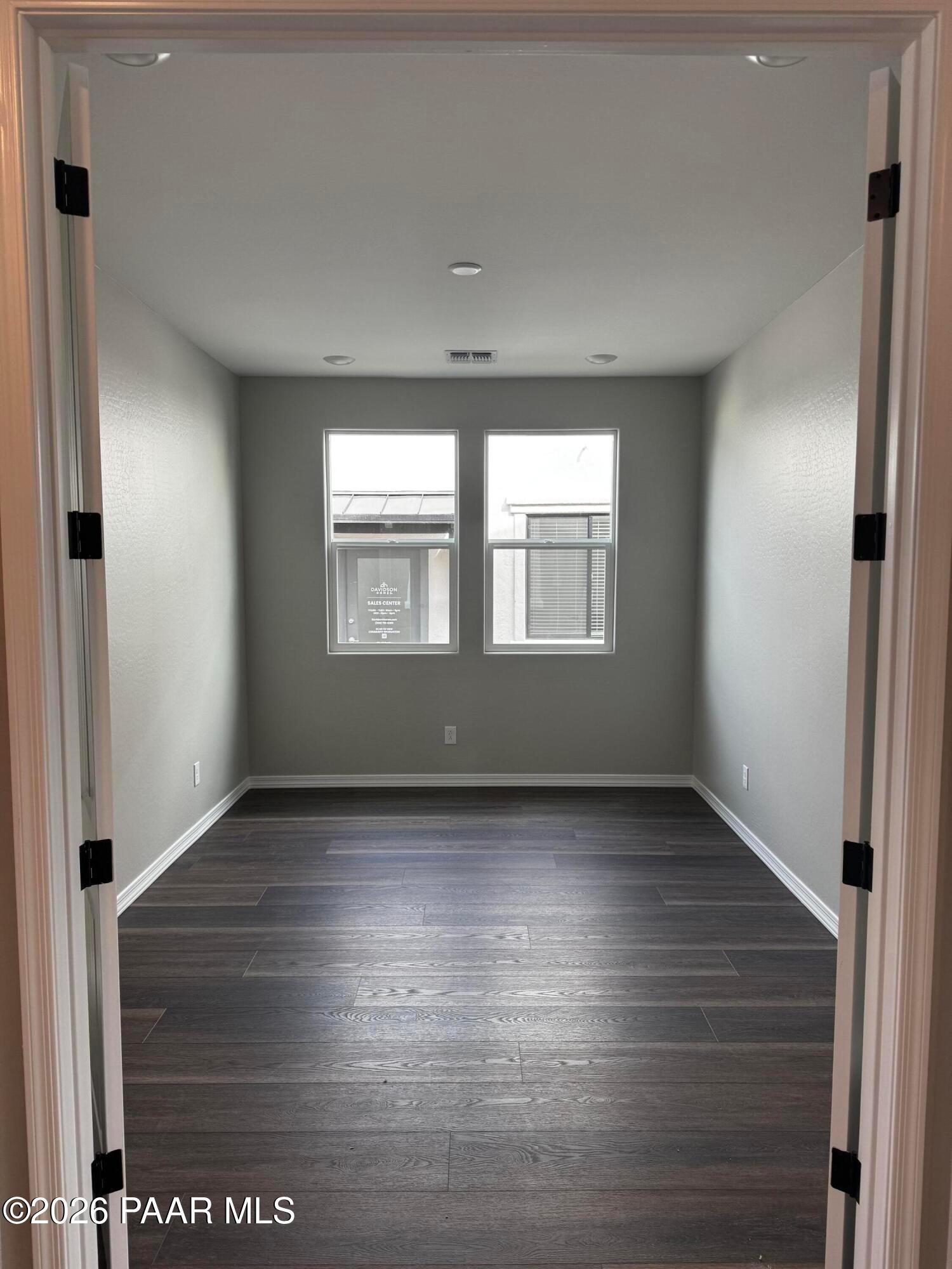 Spacious empty bedroom with light gray walls, large dual windows, blinds, and dark hardwood floors in Davidson Homes Durango II B, Prescott AZ