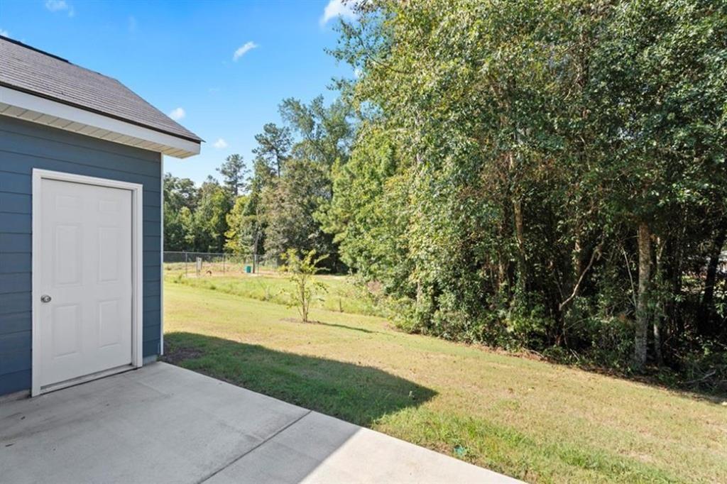 1-car garage with blue door on single-story home, concrete pad, green lawn, and wooded backdrop in Summer Vineyard, Phenix City, Alabama