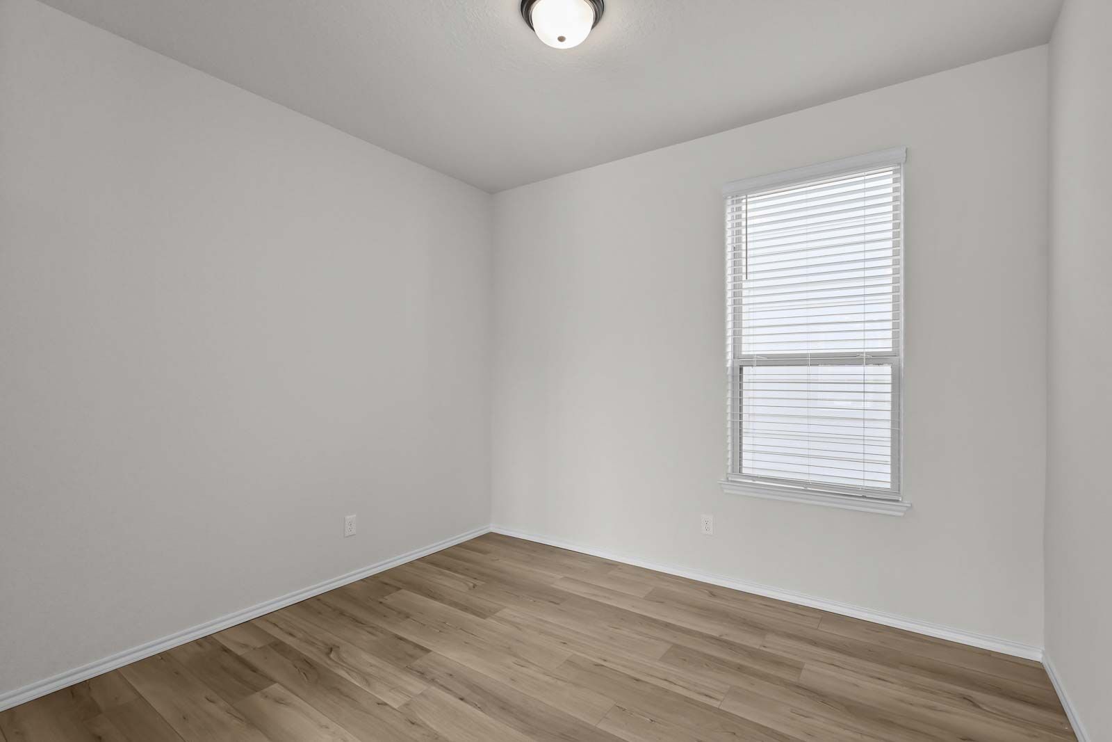 Bright, neutral bedroom in The Florence B home design featuring modern wood-look flooring and a large light-filled window.