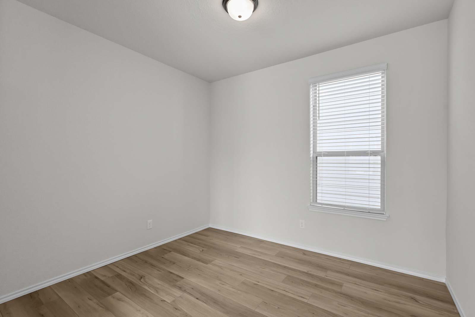 Bright, neutral bedroom in The Florence B home design featuring modern wood-look flooring and a large light-filled window.
