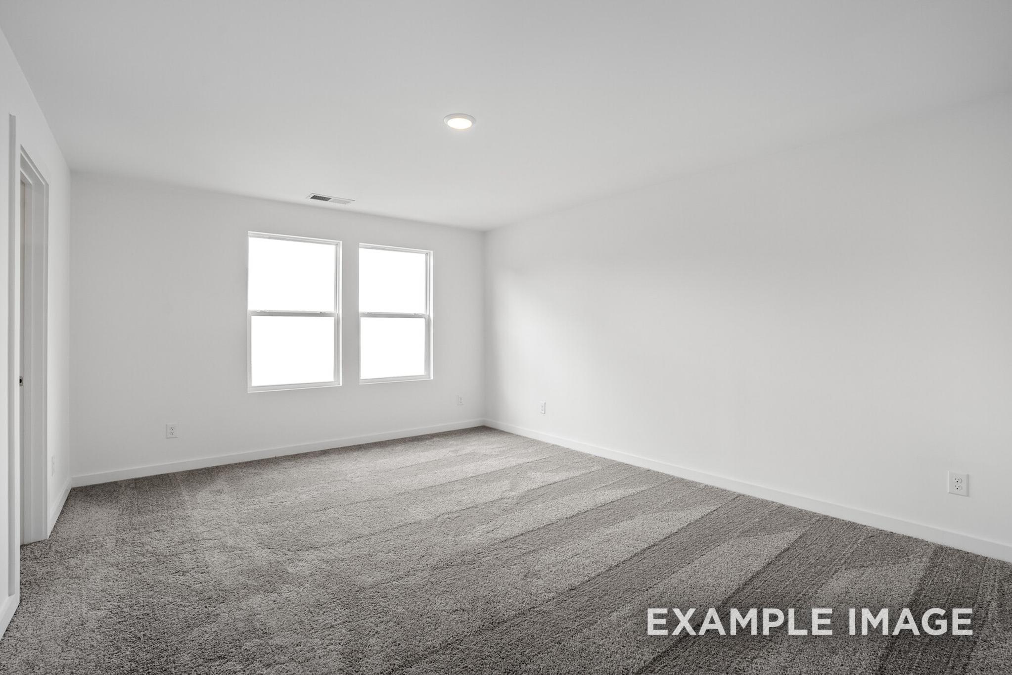 Spacious empty bedroom in The Logan C home design with gray carpet, white walls, double windows, and recessed lighting