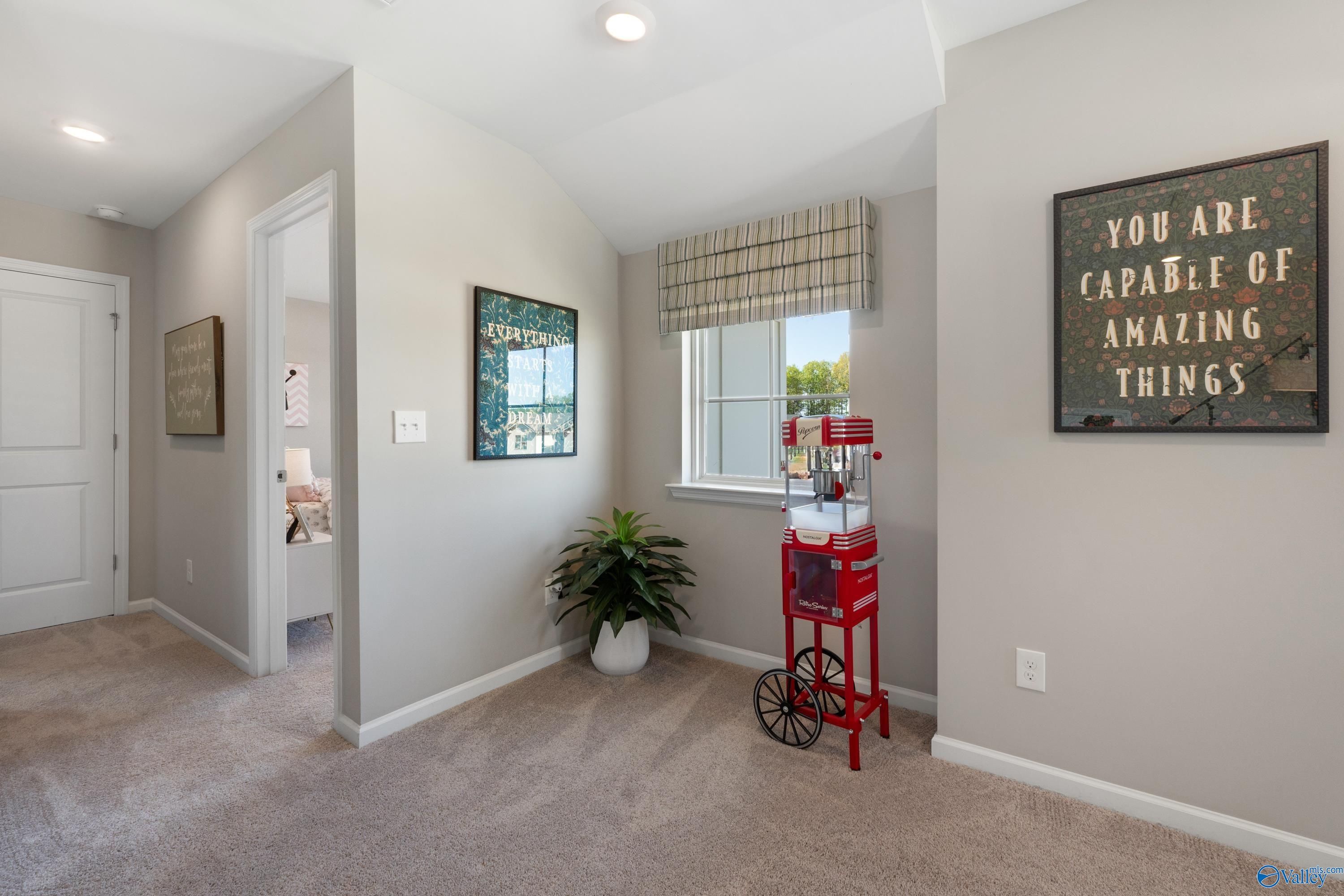 Cozy upstairs loft hallway with gray walls, vintage red popcorn cart, potted plant, and "You Are Capable" wall art in Davidson Homes The Stella, Madison AL