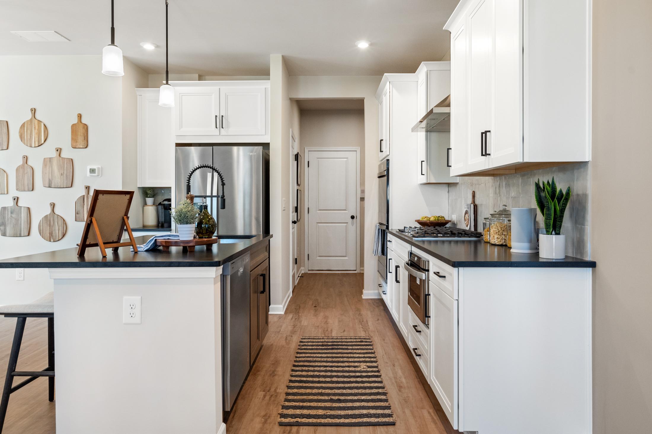 Spacious kitchen in The Marion A with white shaker cabinets, stainless steel appliances, granite island, and open hallway