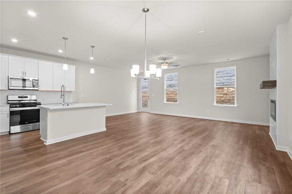 Open-concept kitchen and living area with white shaker cabinets, stainless appliances, island, hardwood floors, and fireplace in Davidson Homes The Marion B, Kennesaw, GA